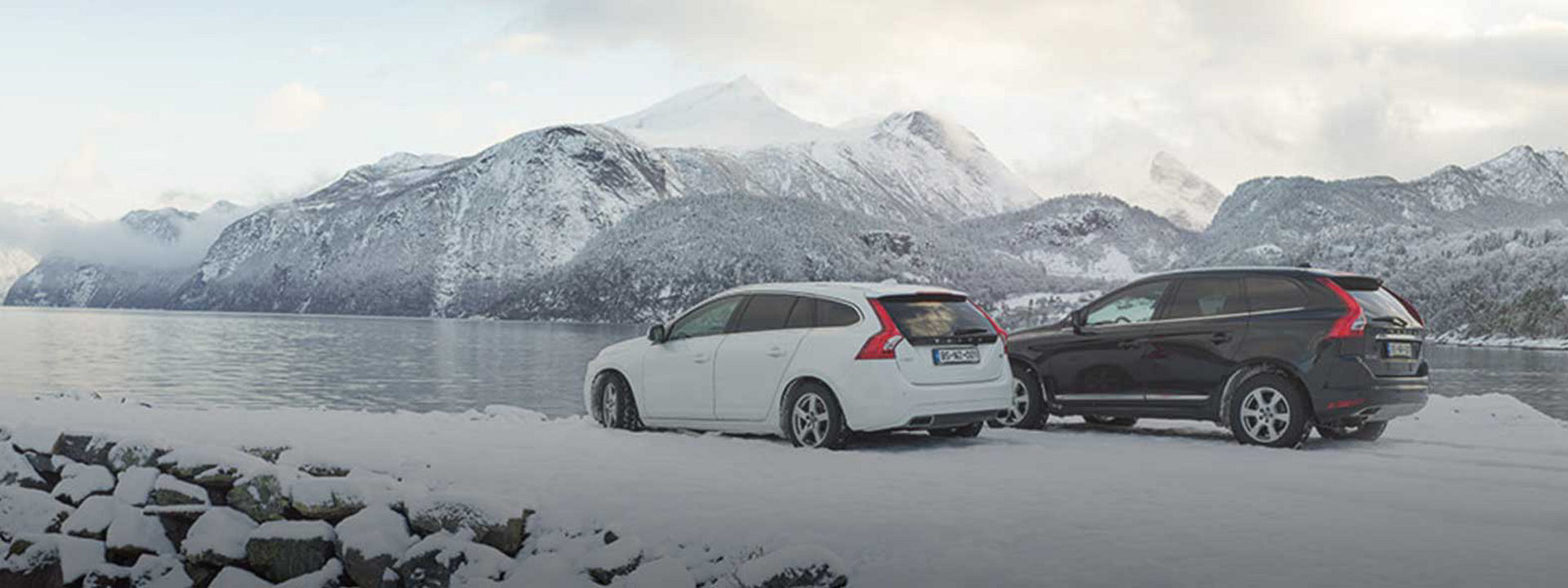 Bilden visar två fordon med Noranza-vinterdäck vid en sjö i ett nordiskt land. 