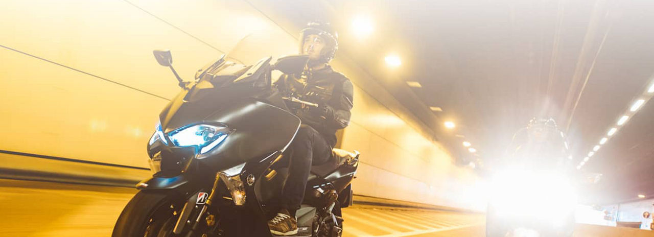 This image shows two people driving scooters in a tunnel with Bridgestone Scooter tyres.