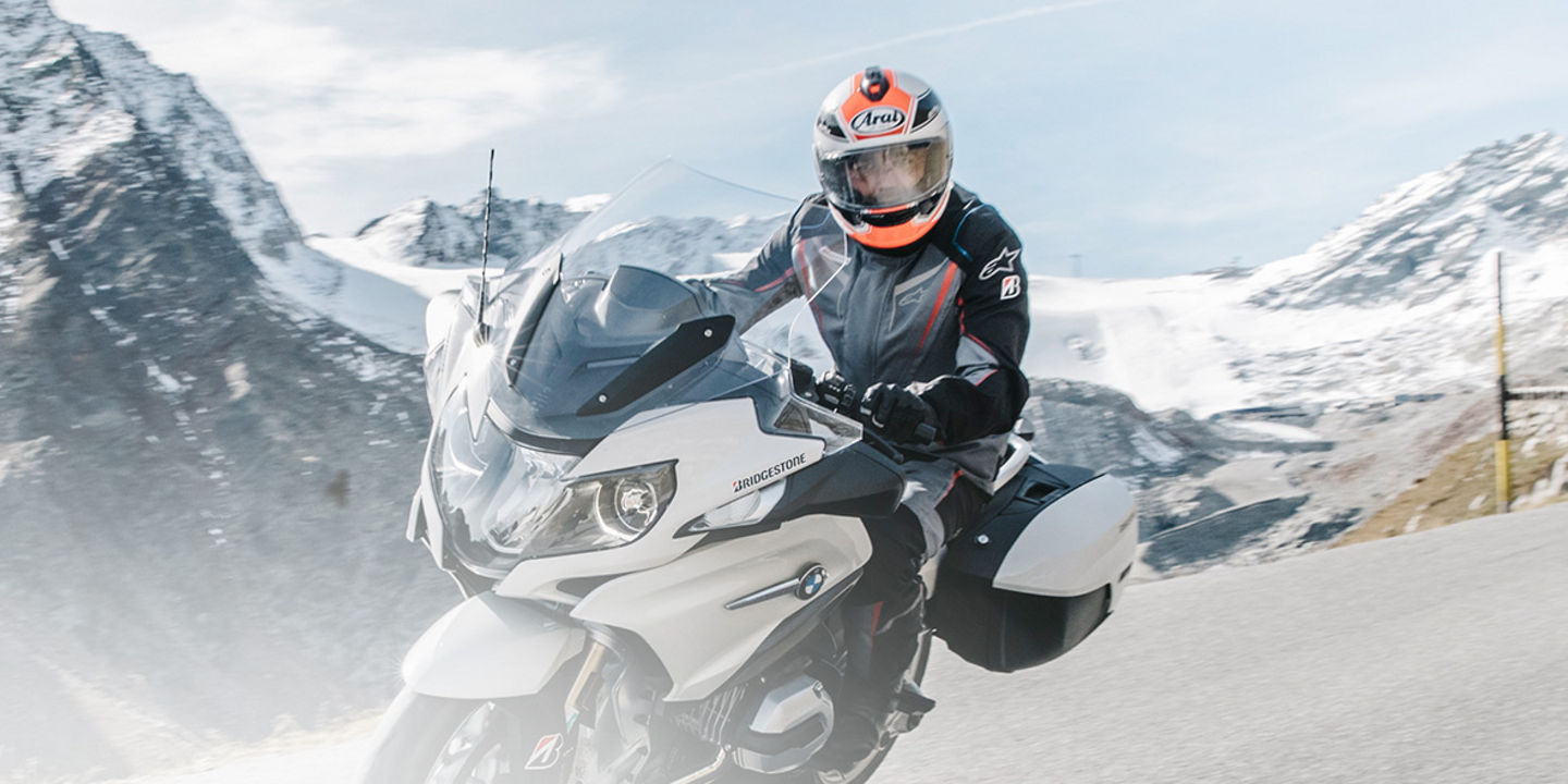 This image shows a motorcyclist riding their motorbike with Bridgestone touring tyres through a scenic road with mountains in the background