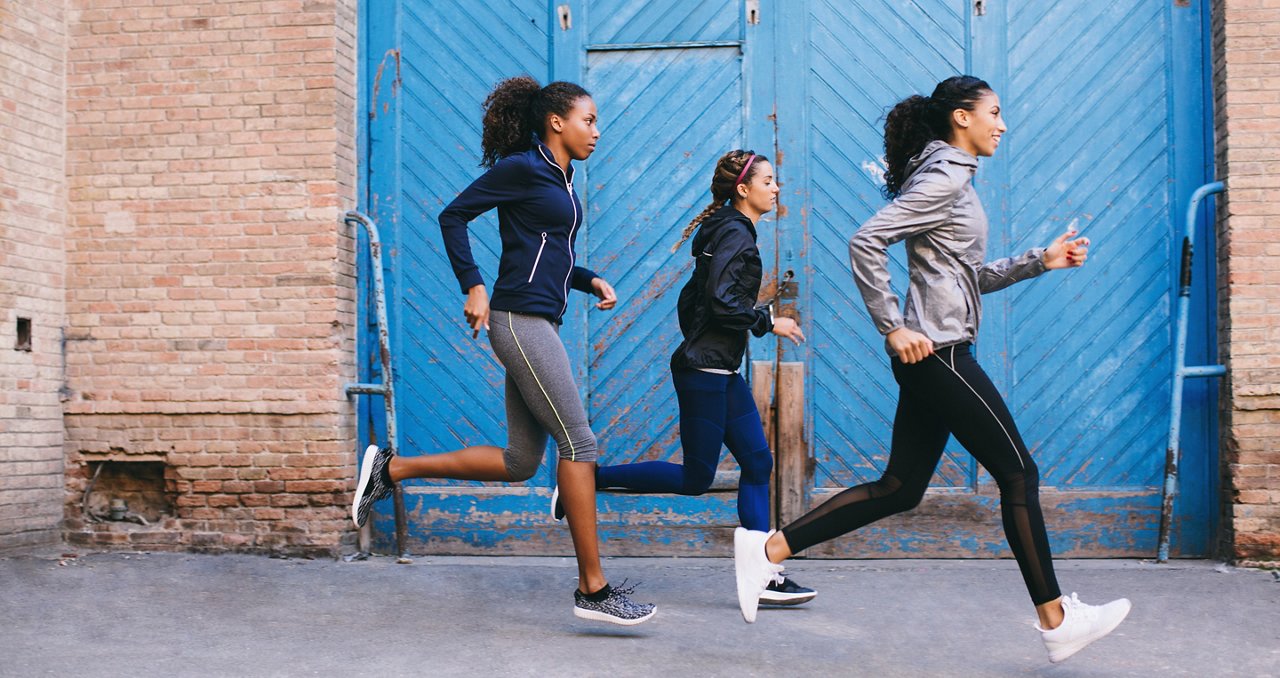 Three women running in front of a warehouse.