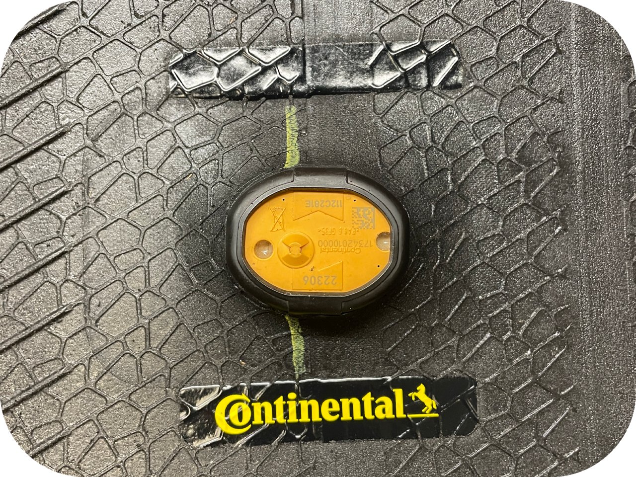 Close-up of a Continental tire tread with an embedded yellow TPMS sensor and a green alignment line.