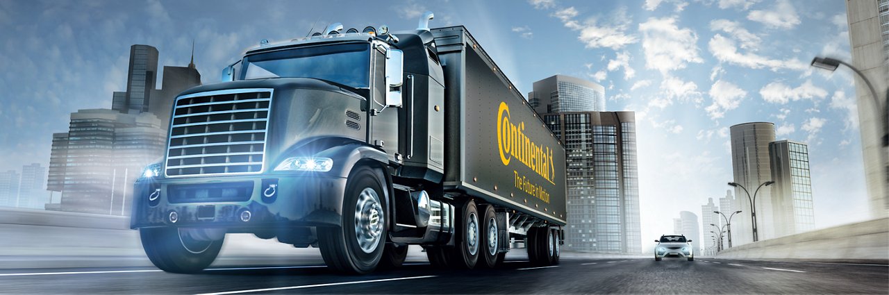 Black Continental semi-truck on urban highway with tall buildings and partly cloudy sky
