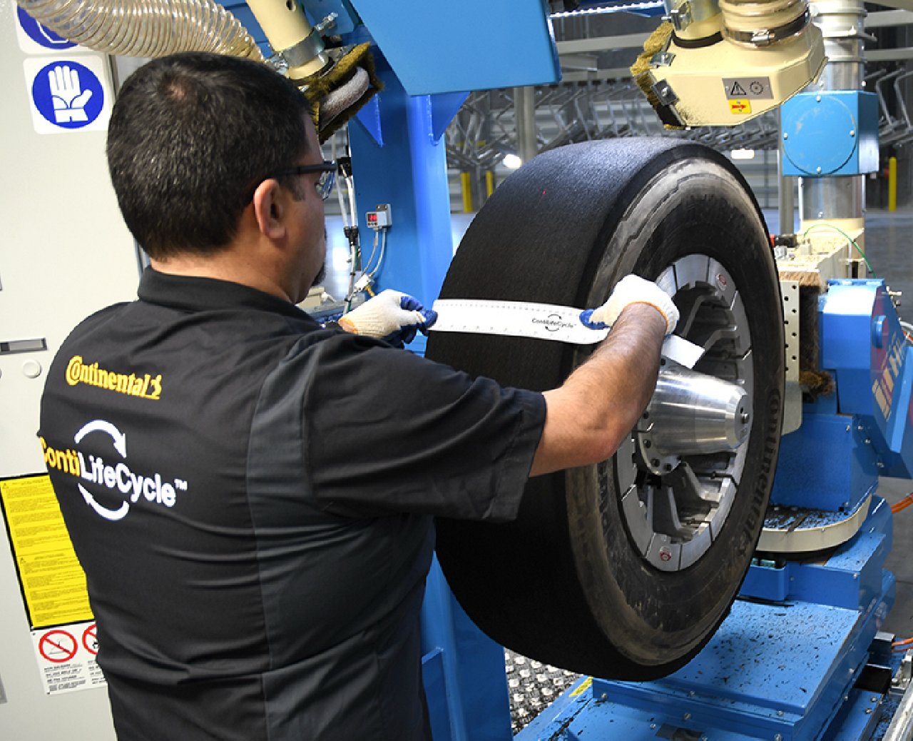 Technician measures a large truck tire with a tape inside a Continental Retread Solutions retreading facility.