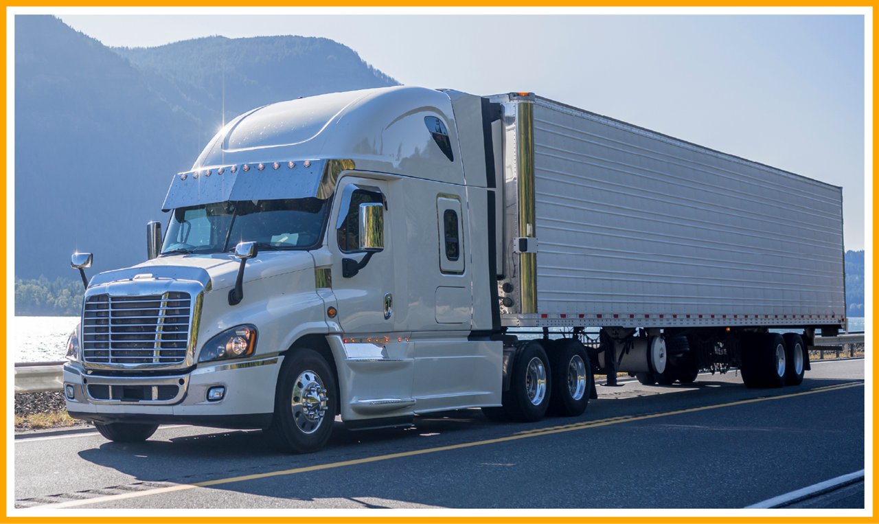 White semi-truck with trailer driving on a scenic road near mountains and a body of water.