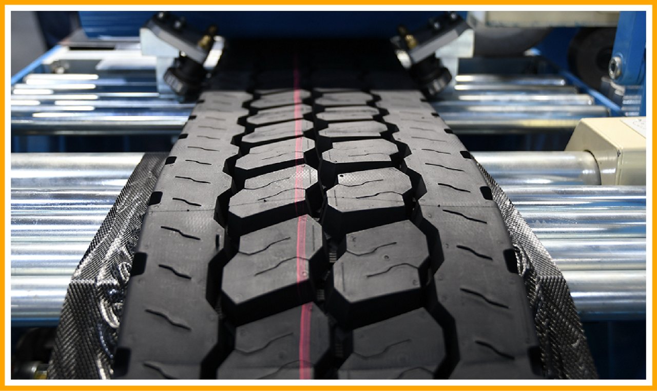 Close-up of a tire tread with hexagonal and rectangular patterns, featuring a red center line, on an industrial machine.