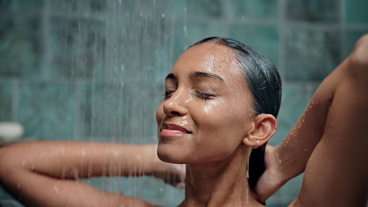 Bathroom, water and woman with washing in shower for haircare, hygiene and happy with cleanliness. Wet, person or cleaning body with smile in home for self care, grooming routine or skincare wellness; Shutterstock ID 2699548617; purchase_order: sito; job: ; client: ; other: 