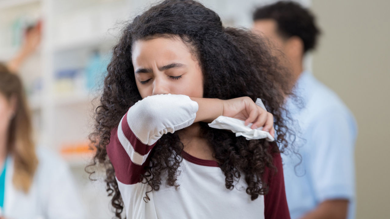 Young mixed race preteen girl sneezes into her arm in pharmacy.