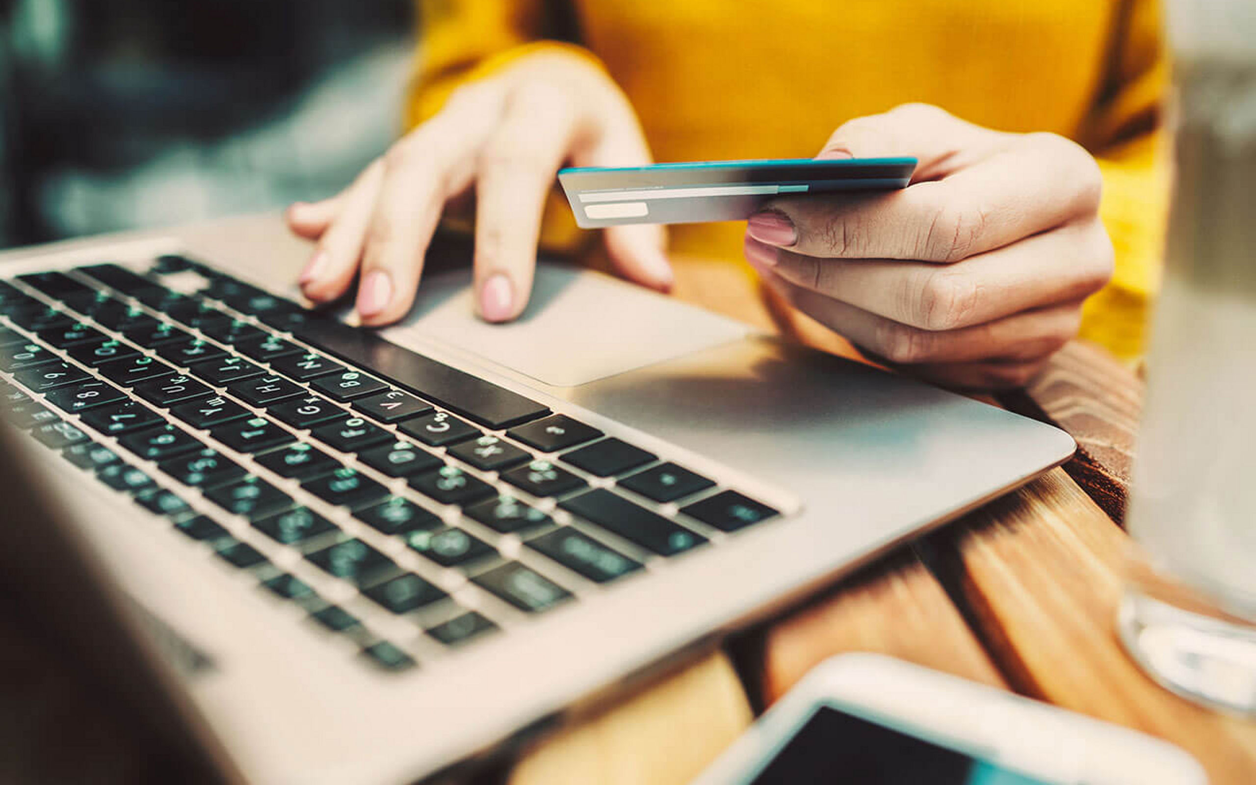 Eine Person sitzt mit Kreditkarte in der Hand vor einem Laptop