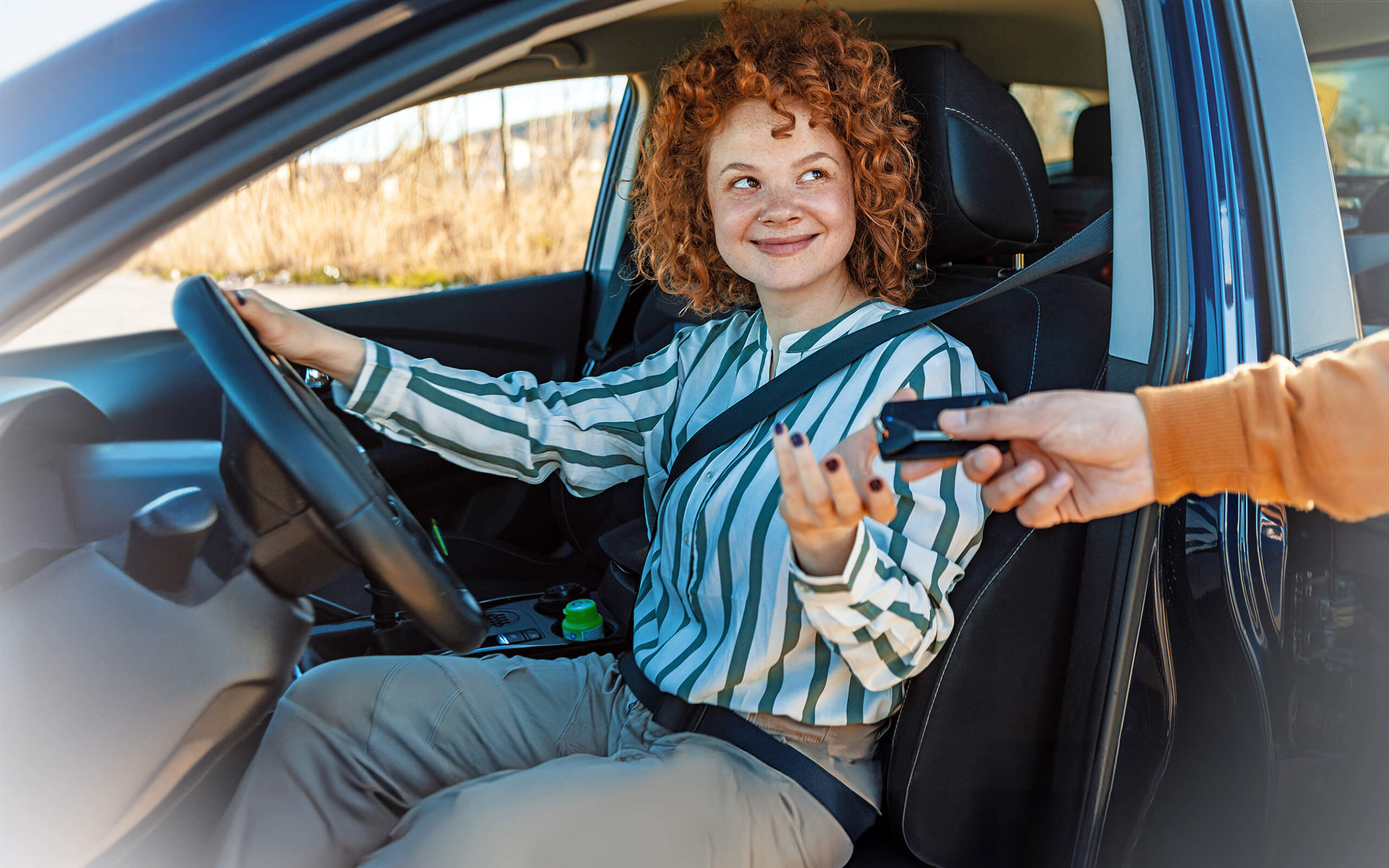 Eine Frau sitzt auf dem Fahrersitz eines Autos und bekommt den Schlüssel überreicht