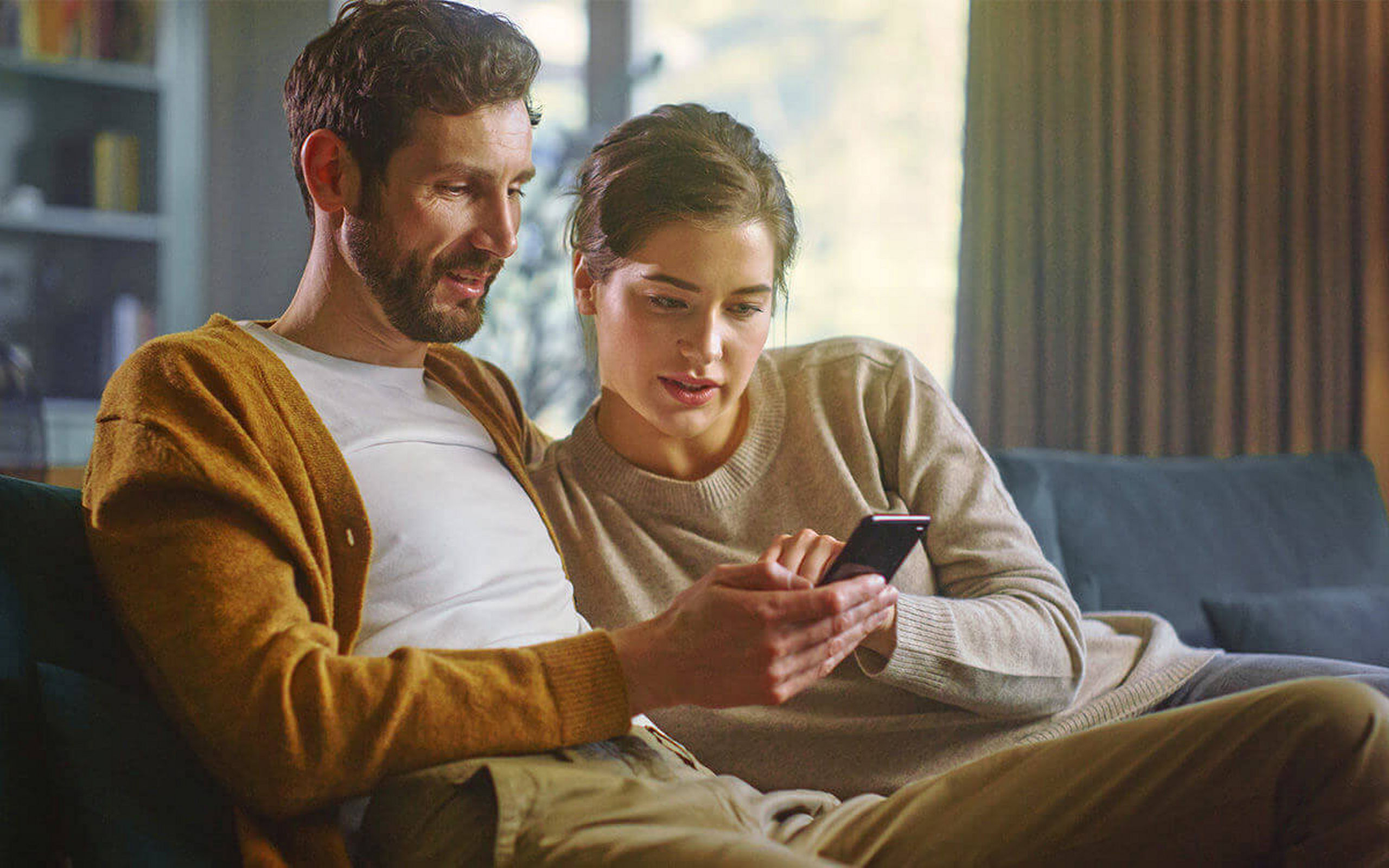 Ein junges Paar sitzt auf einer Couch und sieht auf ein Handy