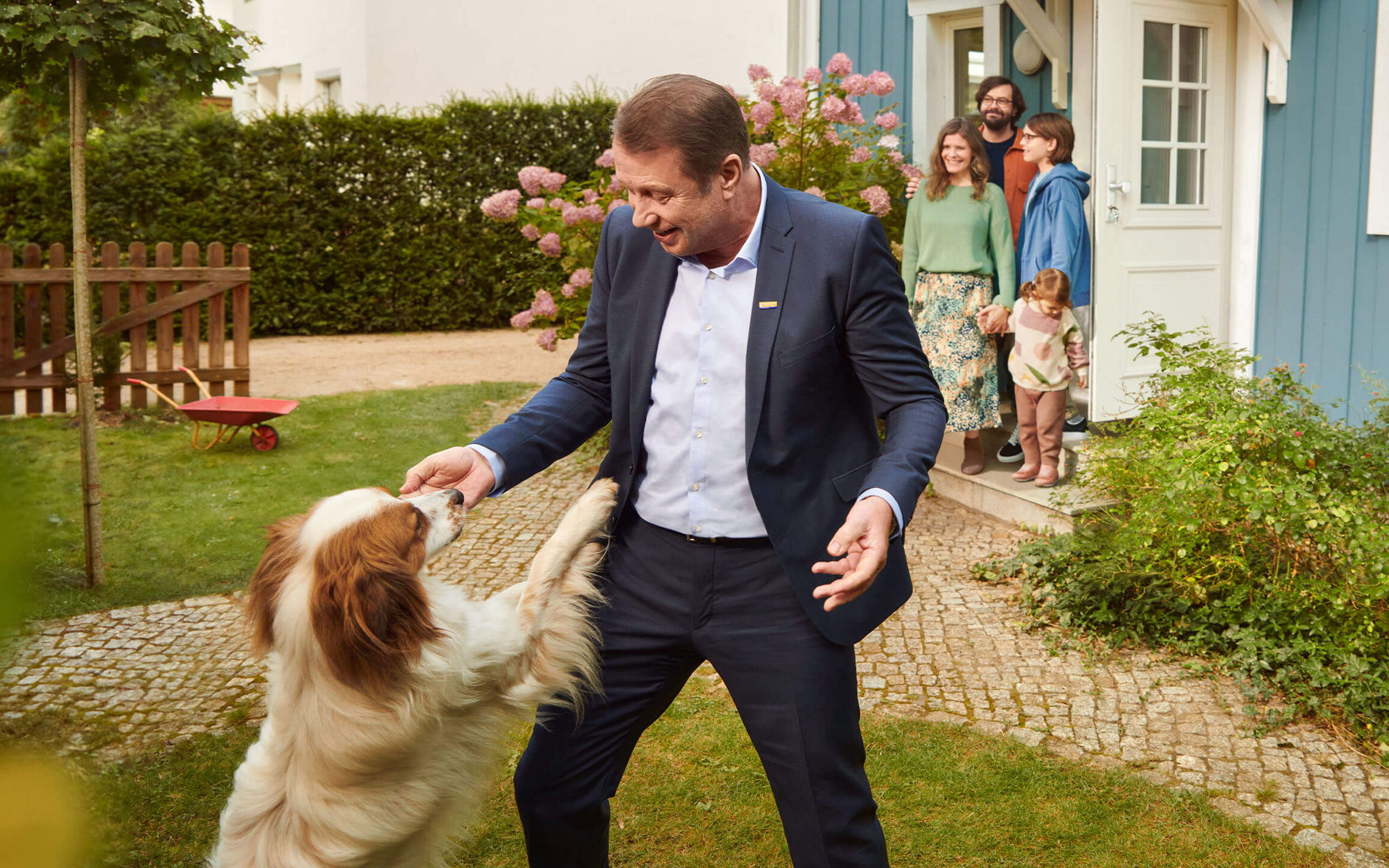 Eine Postbank Berater spielt im Garten eines Eigenheimes mit dem Hund der Besitzer