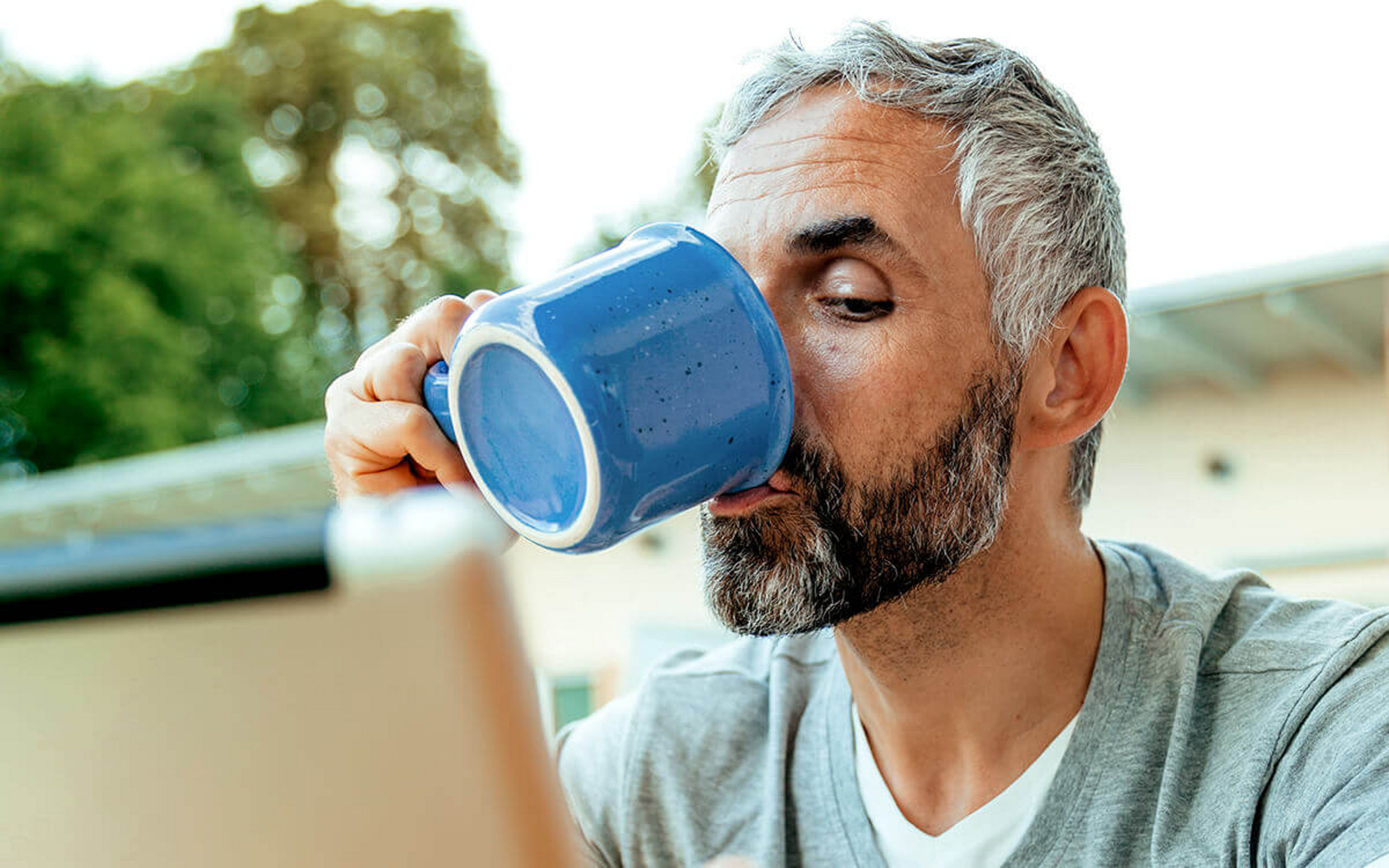 Ein Mann trinkt Kaffee und sieht dabei auf ein Tablet