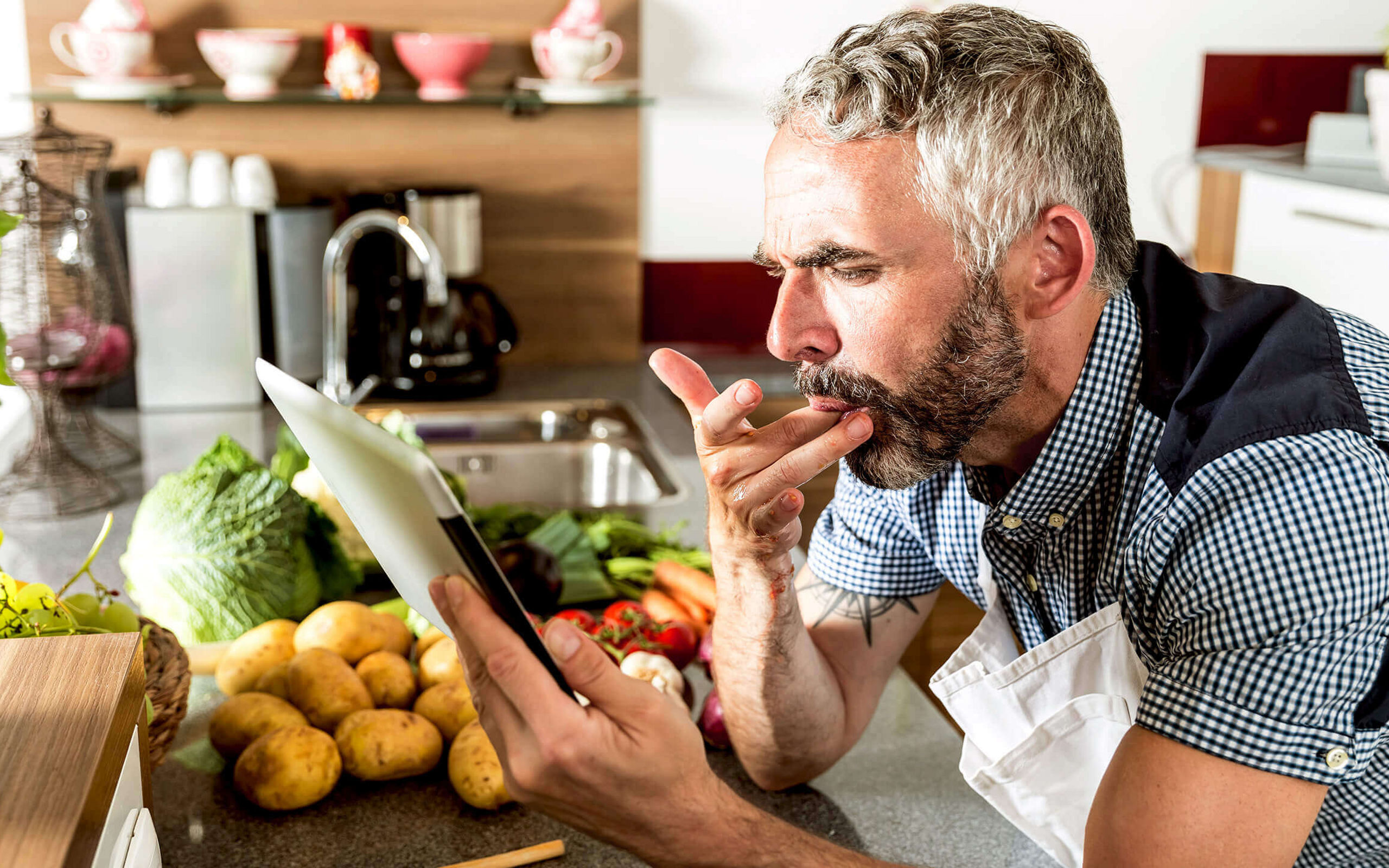 Ein Mann in einer Küche sieht beim Kochen auf ein Tablet