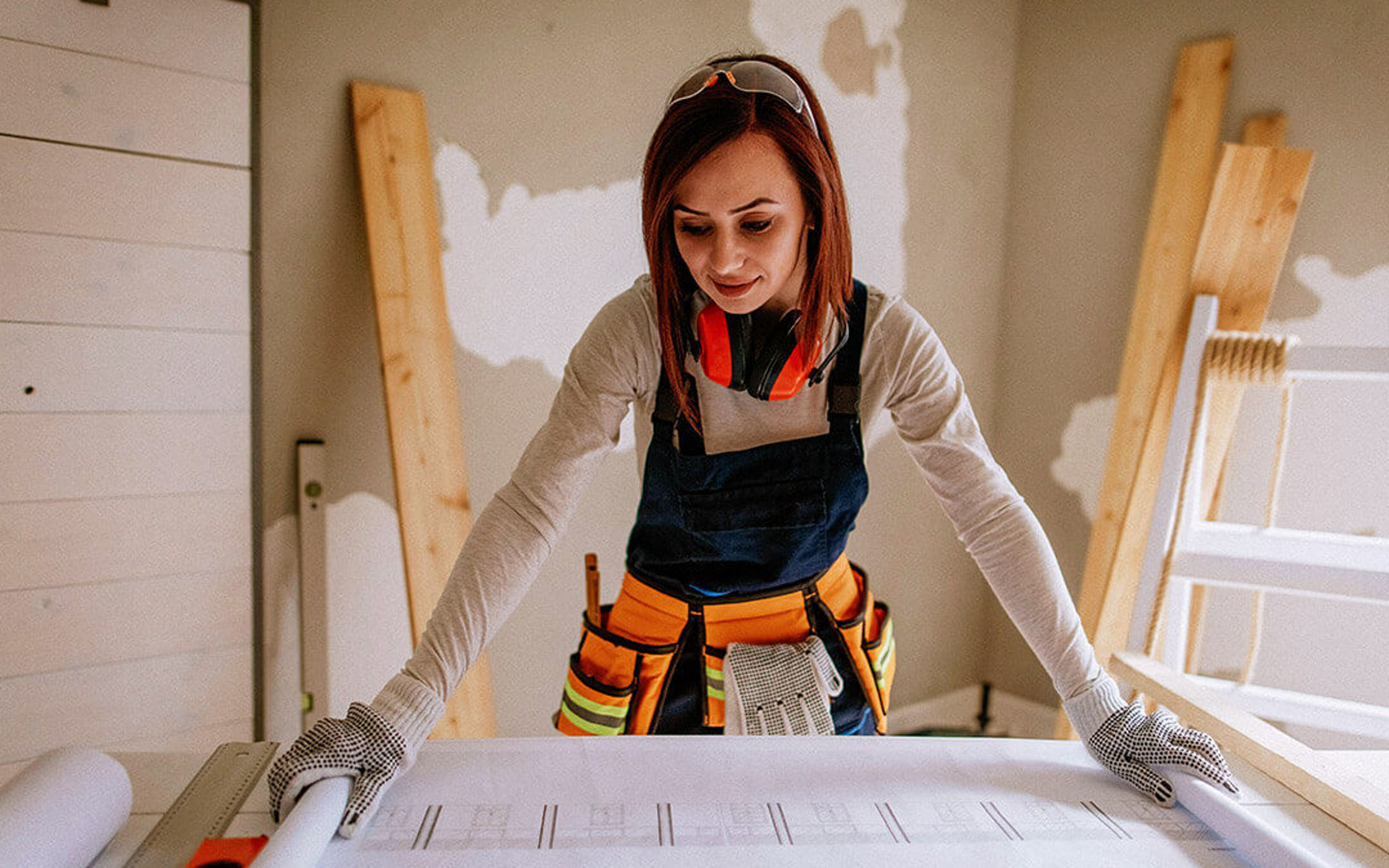 Eine junge Handwerkerin schaut auf einen Bauplan