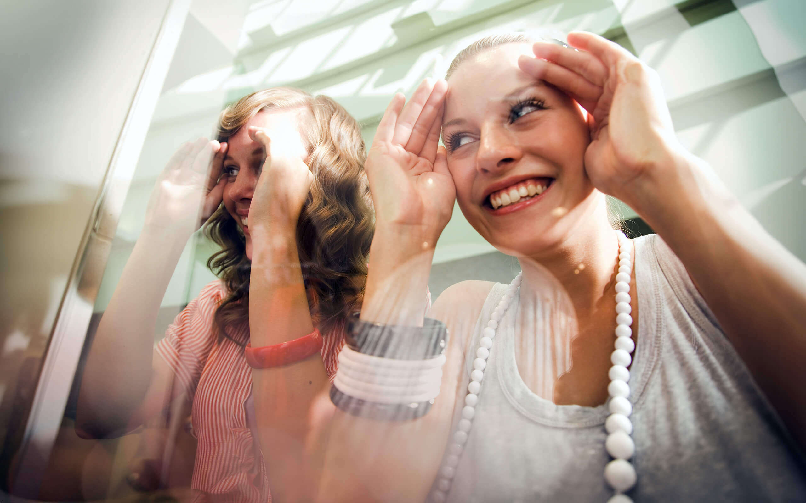 Zwei Frauen schauen fröhlich durch eine Schaufensterscheibe