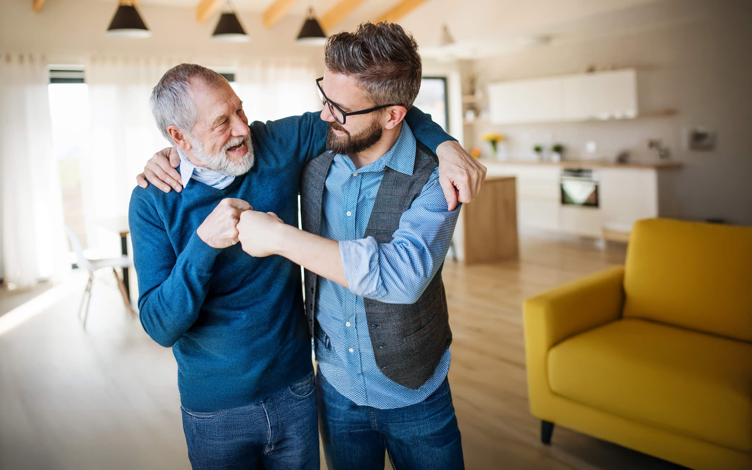 Zwei Herren aus zwei Generationen stehen in einer Wohnküche und machen den "Faustgruß".