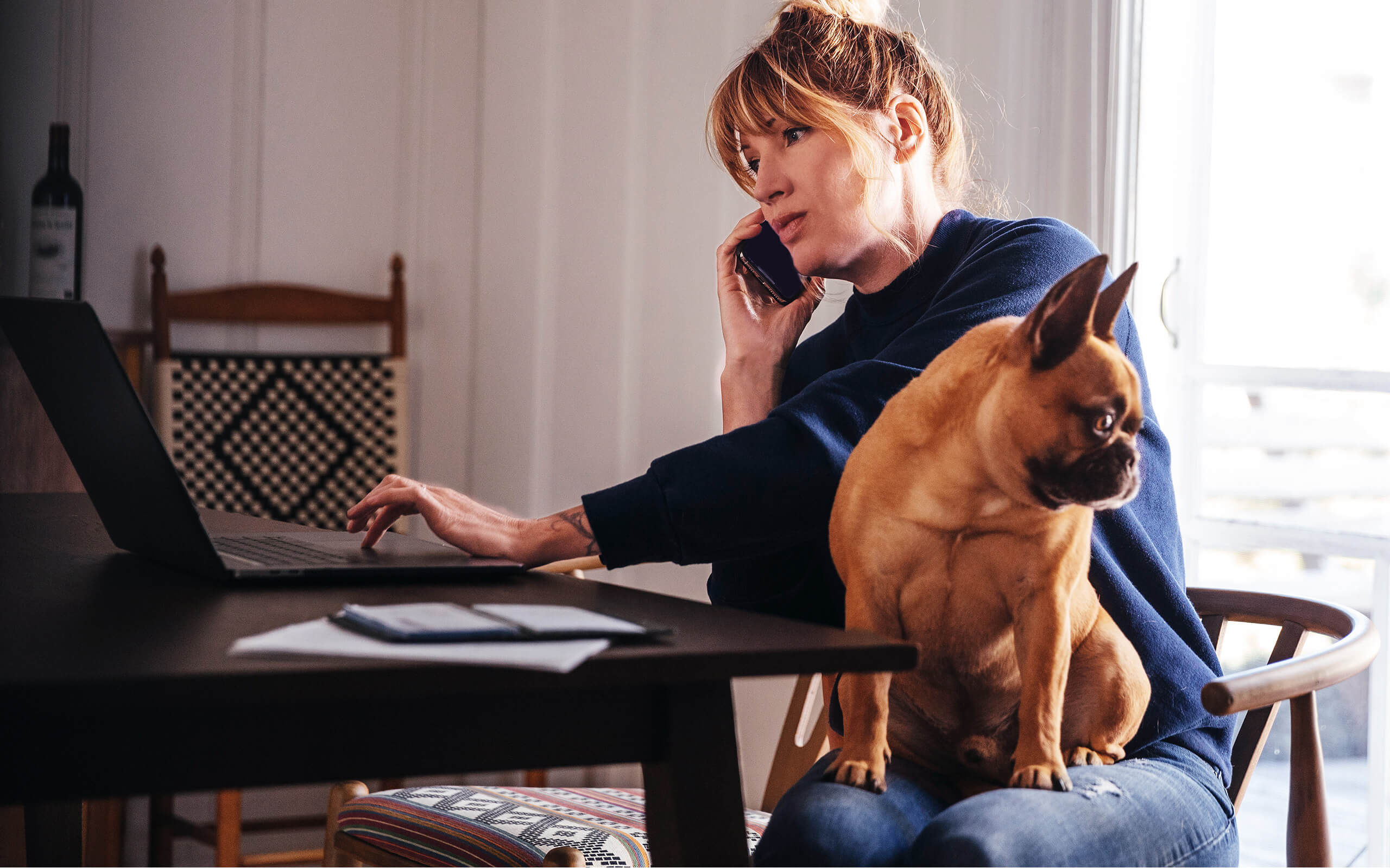 Eine Frau mit und auf dem Schoß telefoniert und tippt nebenbei am Laptop