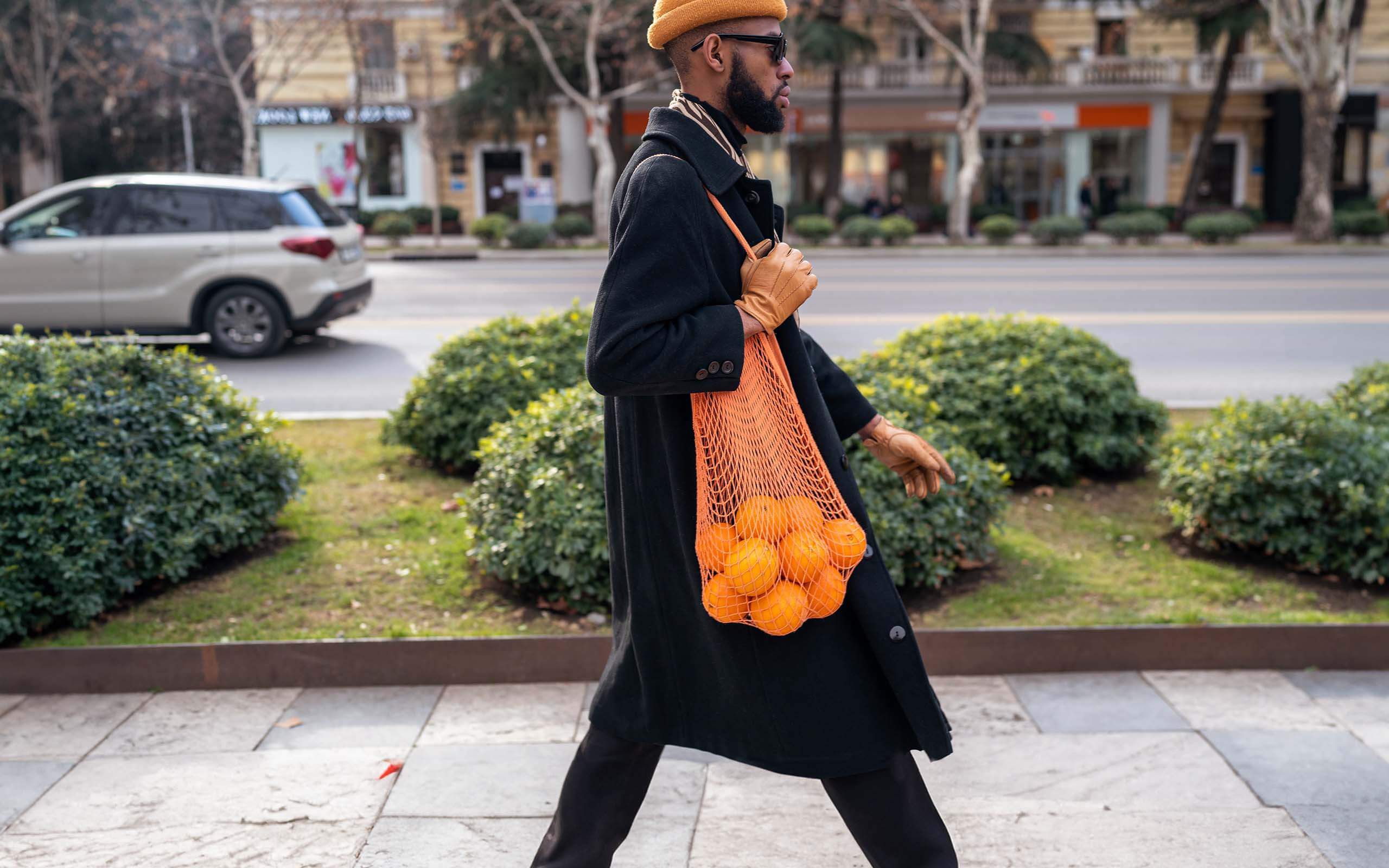 Ein Mann läuft mit einem Einkaufsnetz voller Orangen einen Gehweg entlang