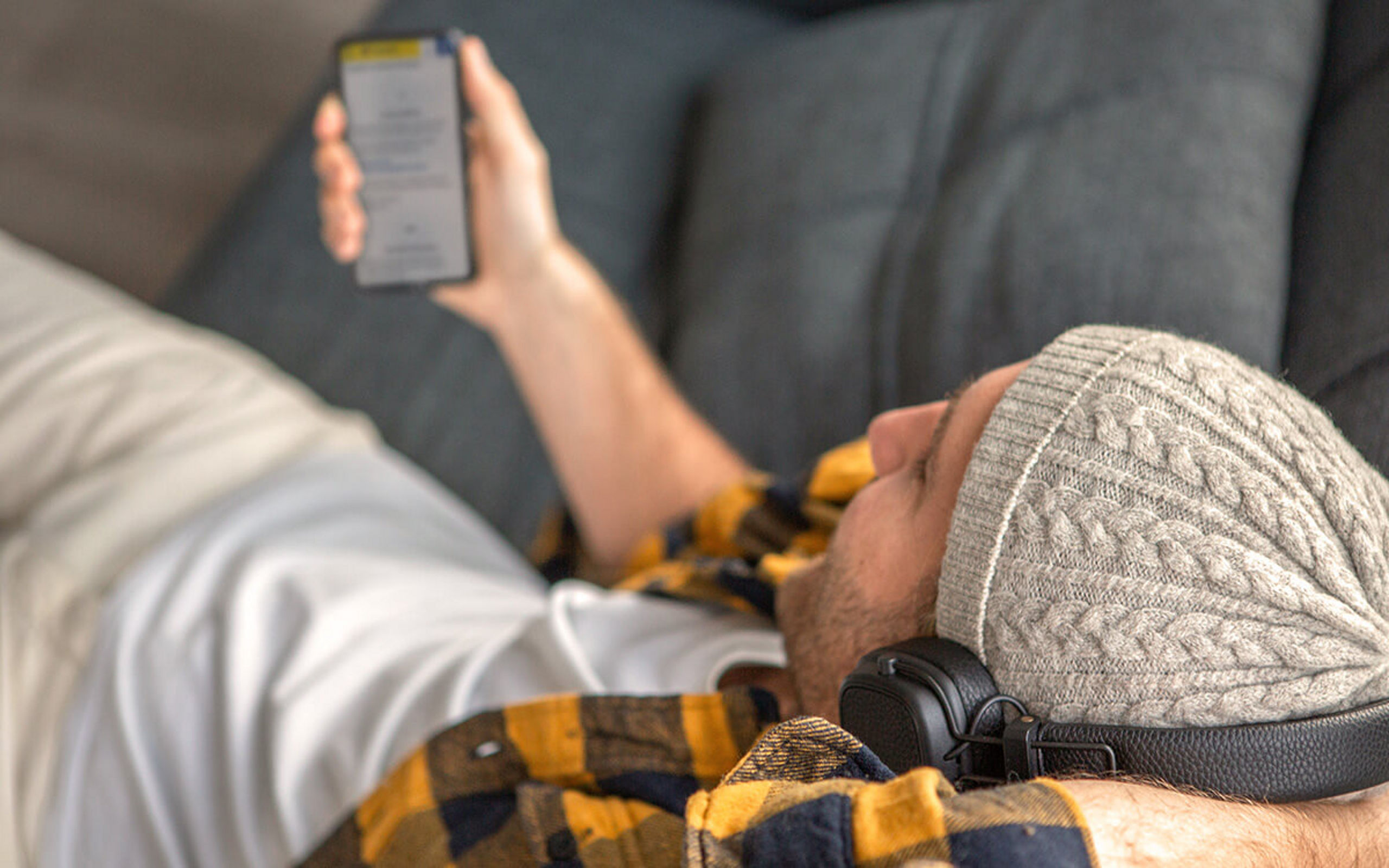 Ein junger Mann liegt auf der Couch und schaut auf sein Handy