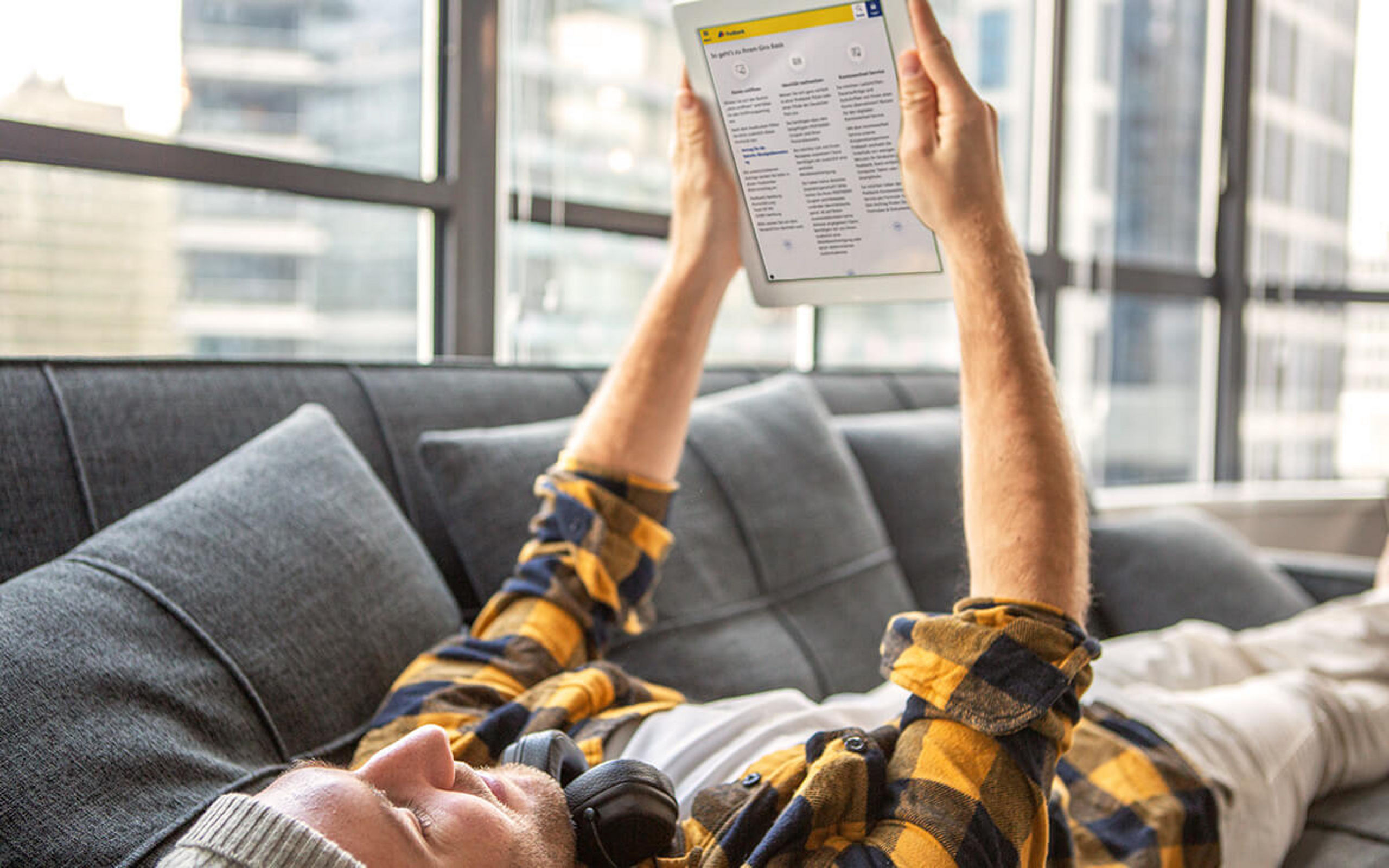 Ein junger Mann liegt auf der Couch und schaut auf sein Tablet