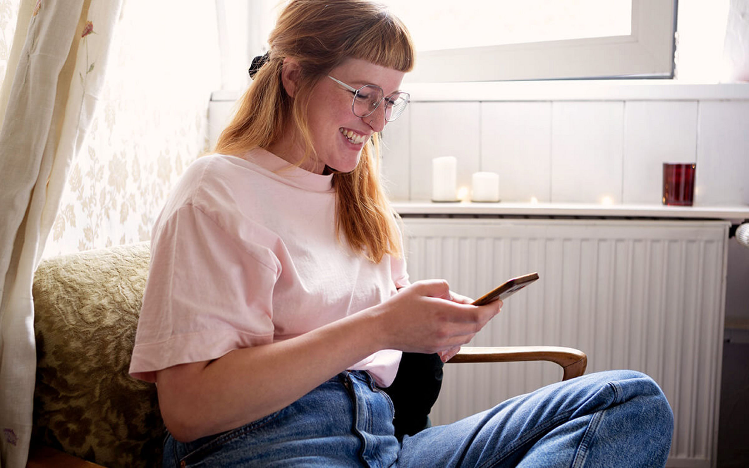 Eine junge Frau sieht auf ihr Handy und lächelt