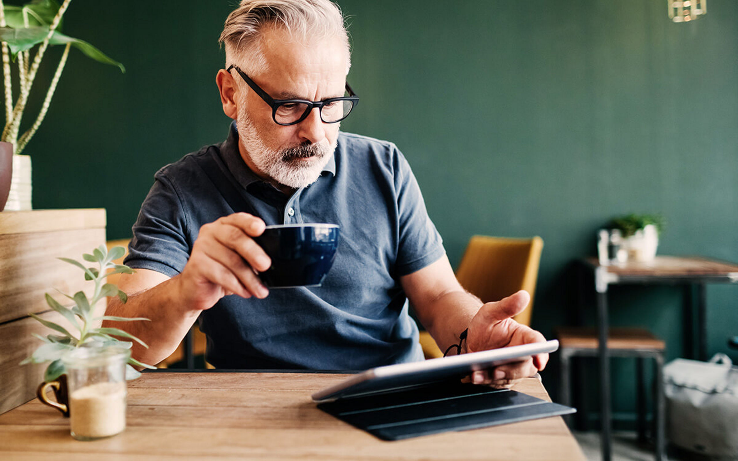 Ein Mann schaut auf sein Tablet und trinkt dabei einen Kaffee