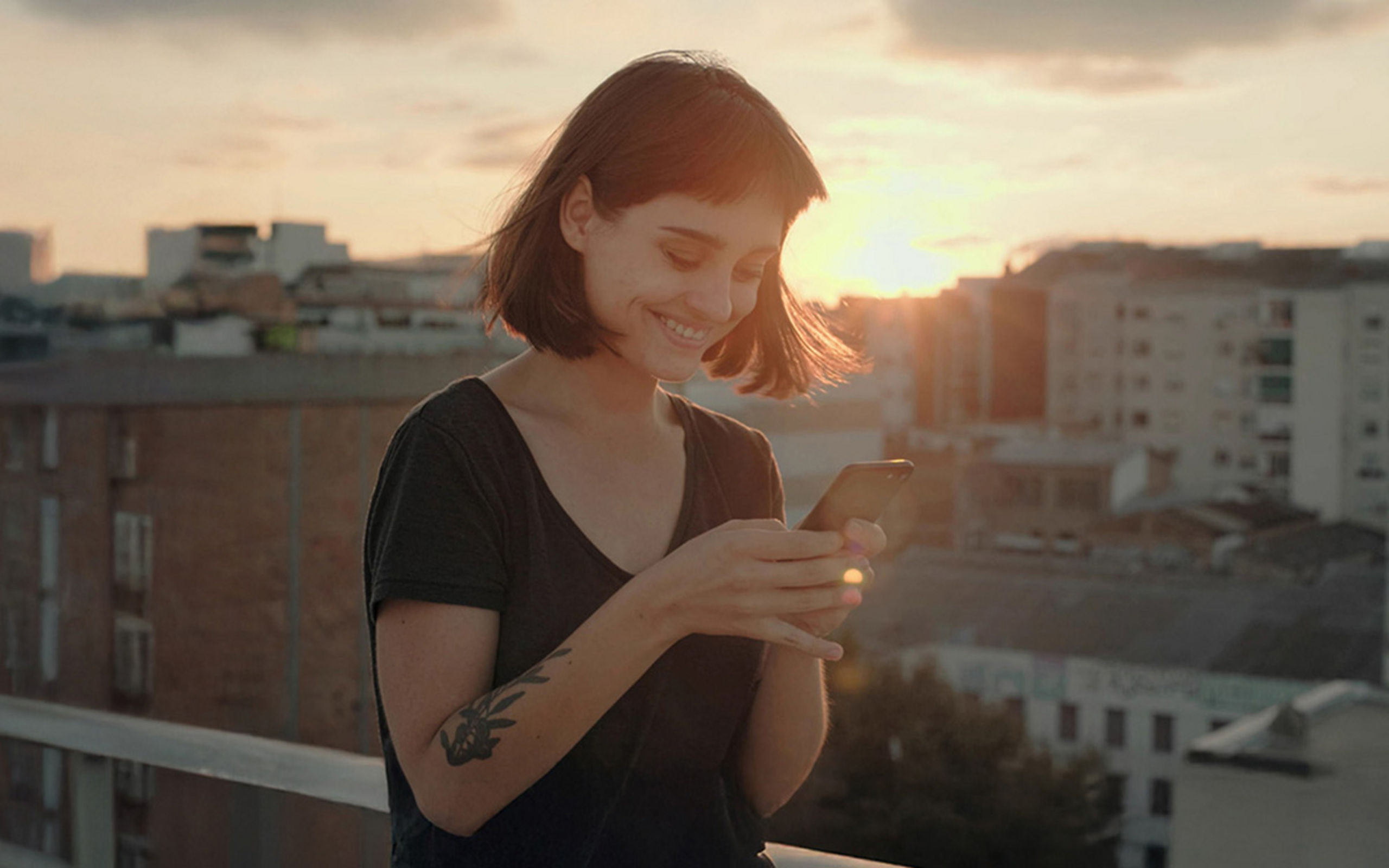 Eine Frau steht in der Abendsonne auf einer Terrasse und  bedient Ihr Smartphone