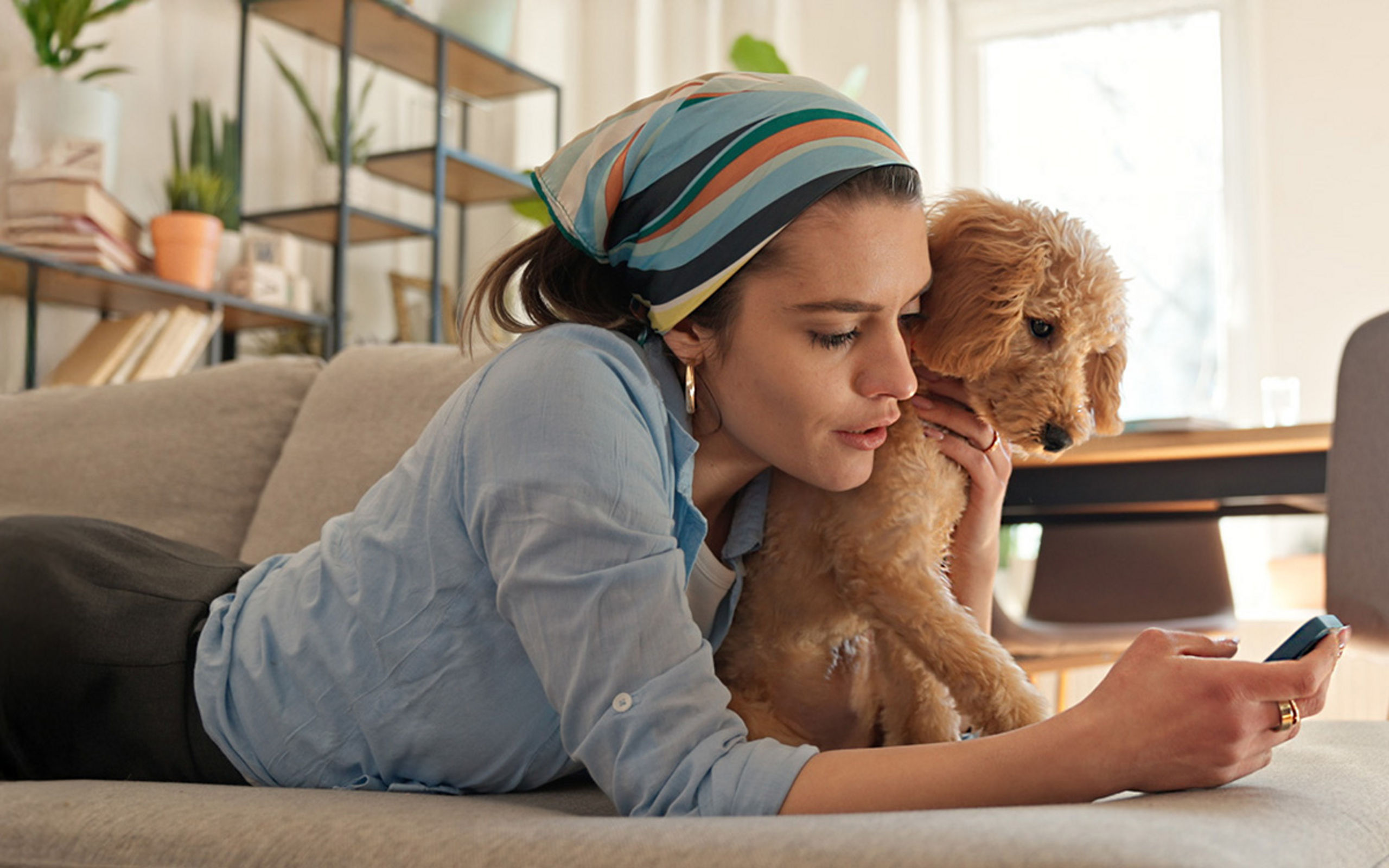 Eine Frau liegt mit ihrem Hund auf der Couch und bedient Ihr Smartphone