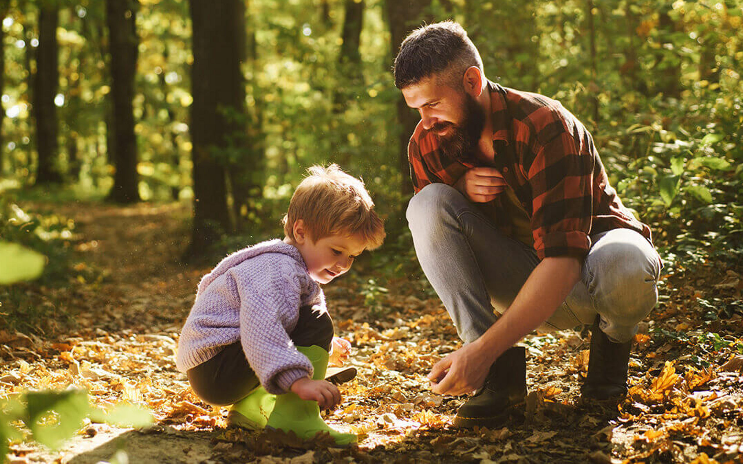 Ein Mann und ein Kind im Wald hocken auf dem Waldboden und sehen sich Blätter an