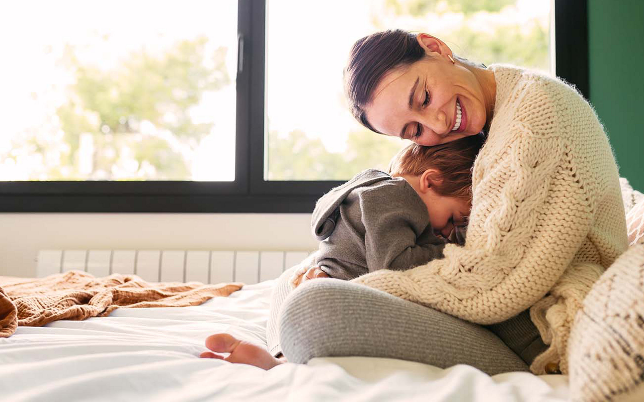 Eine junge Mutter kuschelt mit ihrem Sohn im Bett