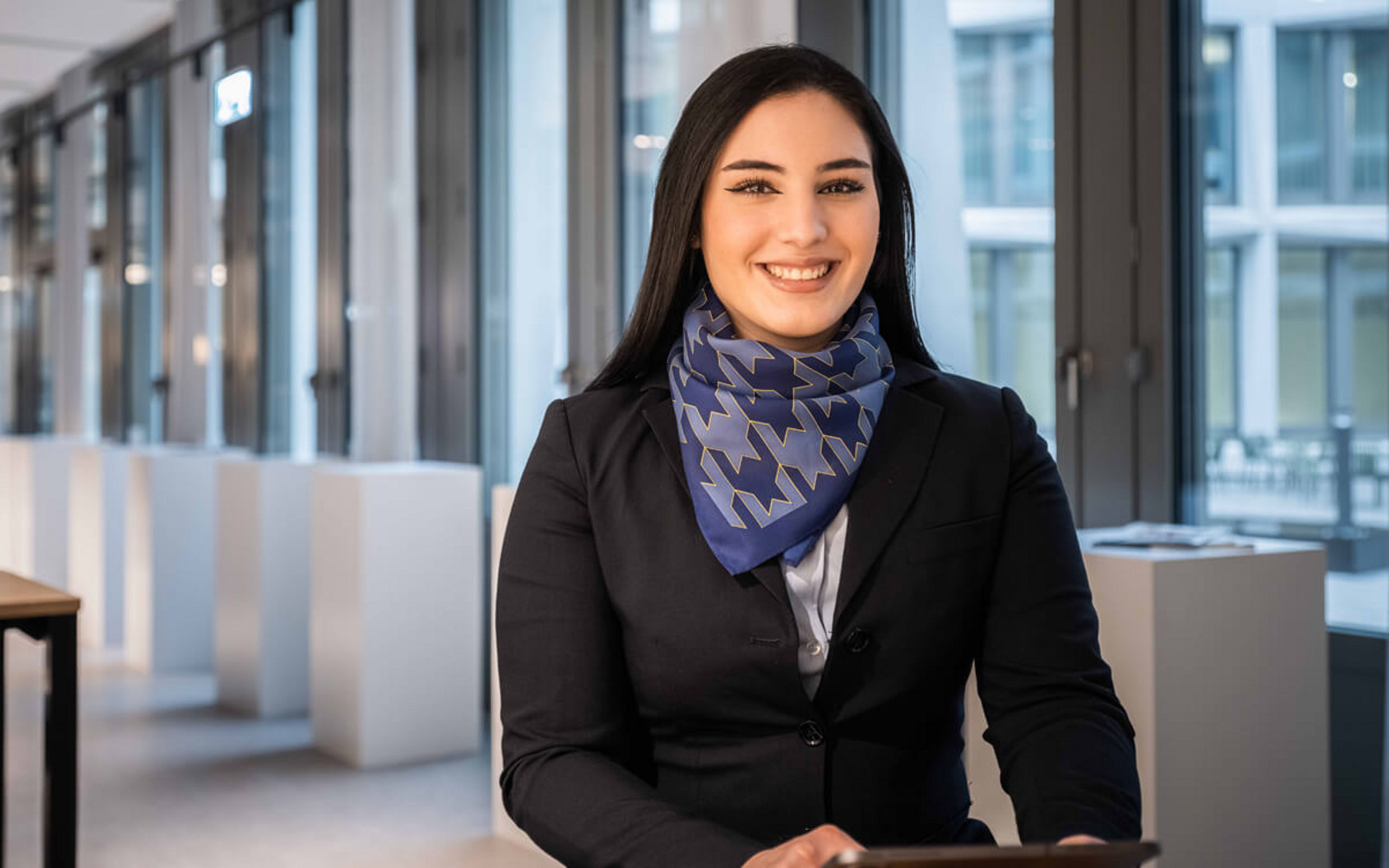 Eine junge Dame sitzt mit Tablet an einem Schreibtisch und lächelt