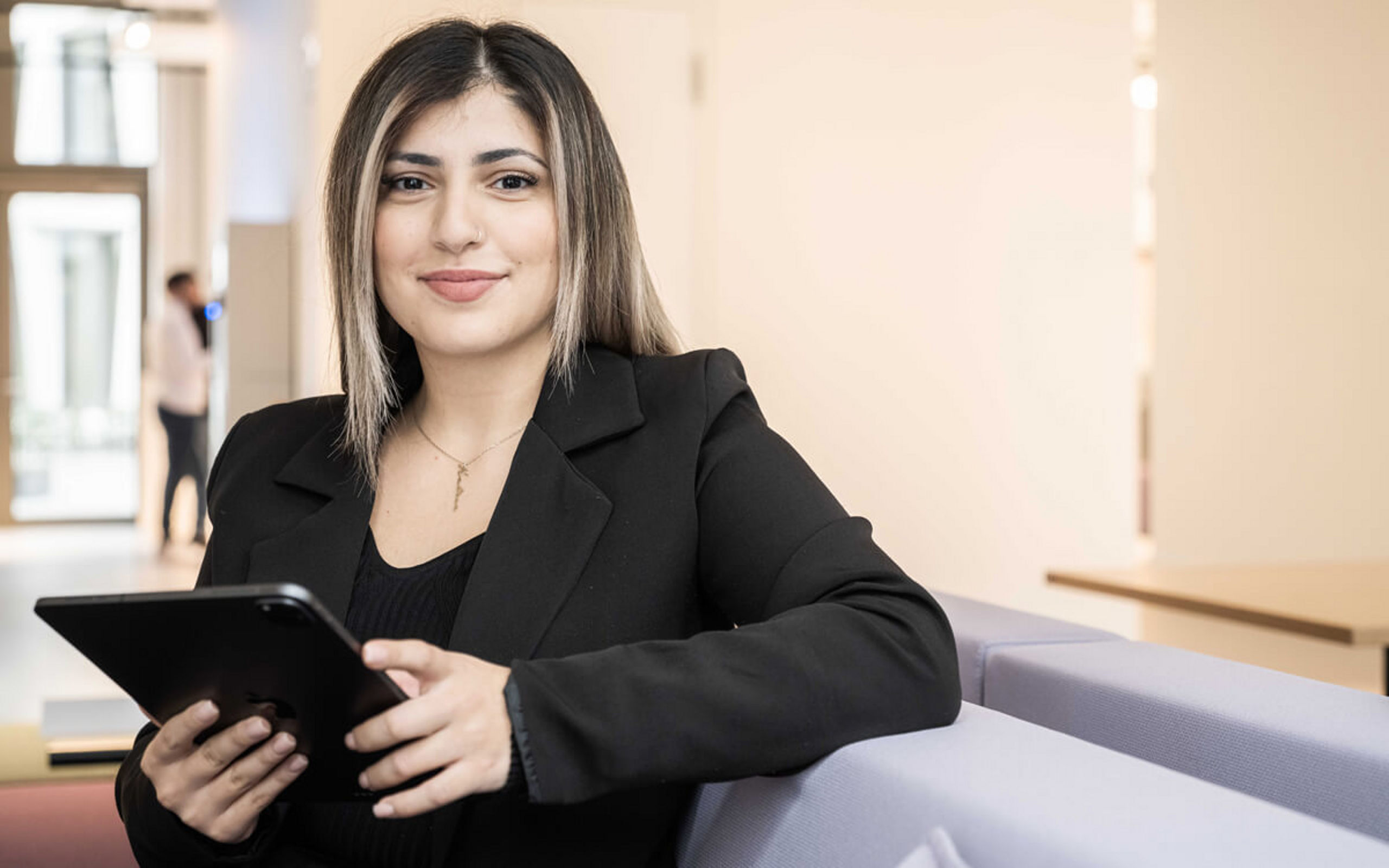 Eine junge Frau mit Tablet in der Hand sitzt auf einem Sofa