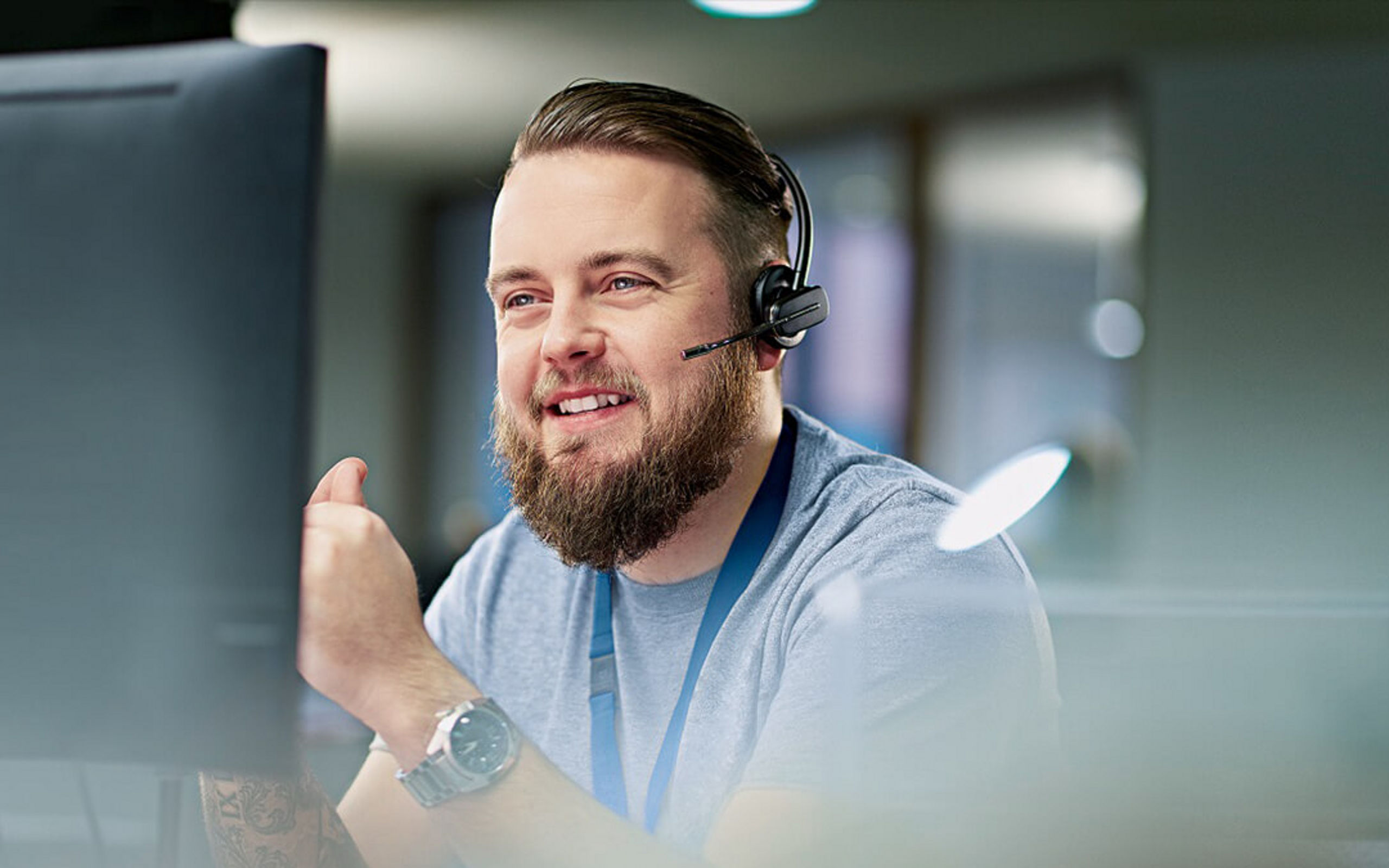 Eine junger Mann mit Headset schaut auf einen Monitor und führt ein Telefongespräch