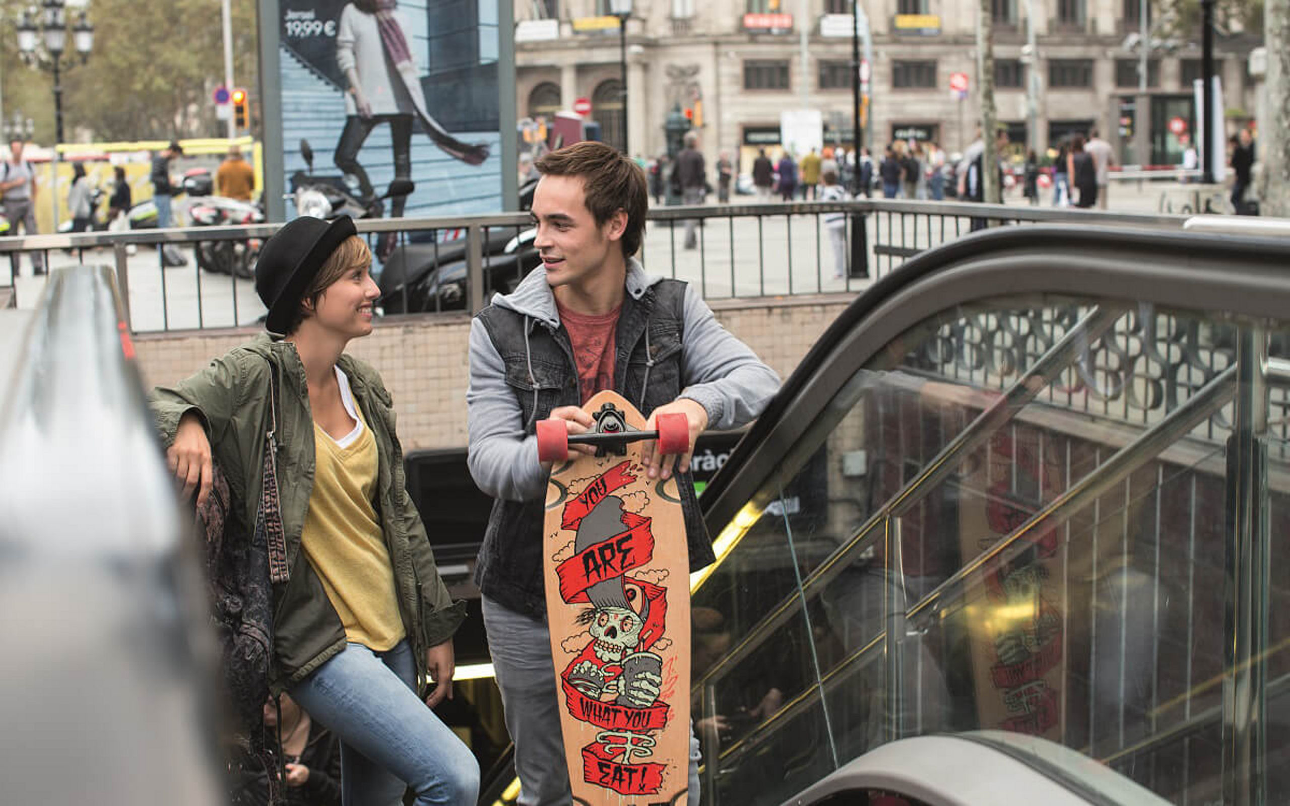 Ein junges Paar steht mit einem Skateboard auf einer Rolltreppe und verlässt einen U-Bahn-Station