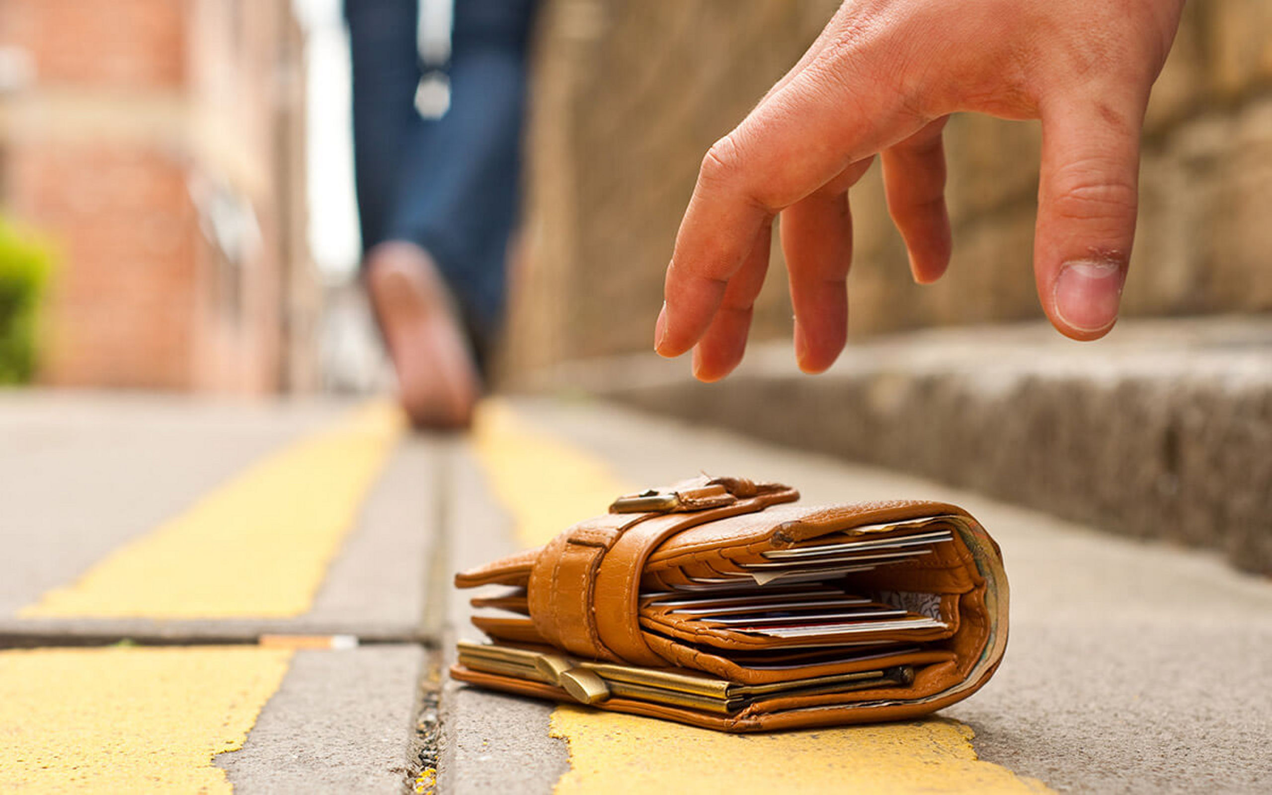 Eine Hand greift nach einem verloren Portemonnaie, welches auf der Straße liegt