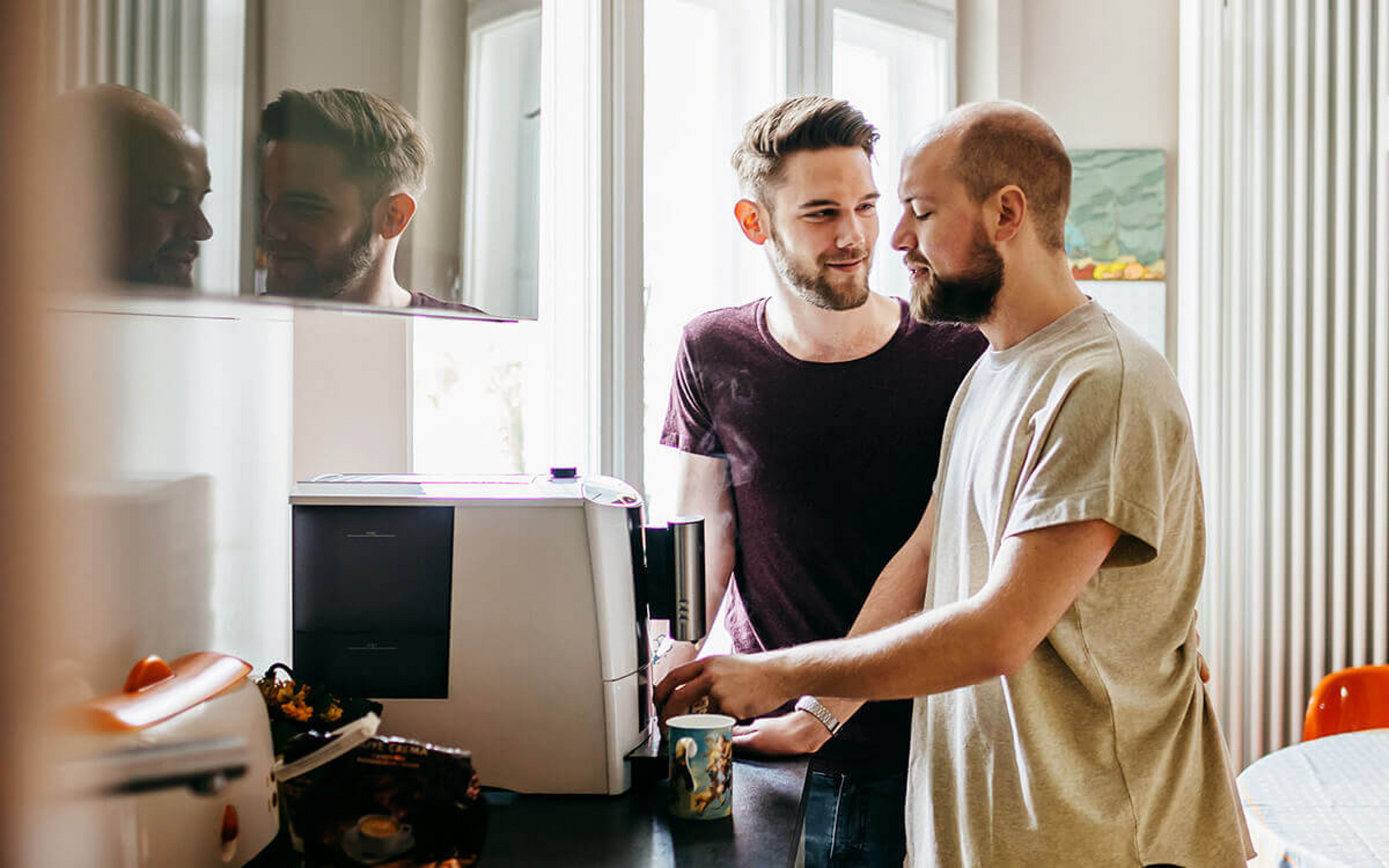 Zwei junge Männer stehen an einem Kaffeeautomat in der Küche