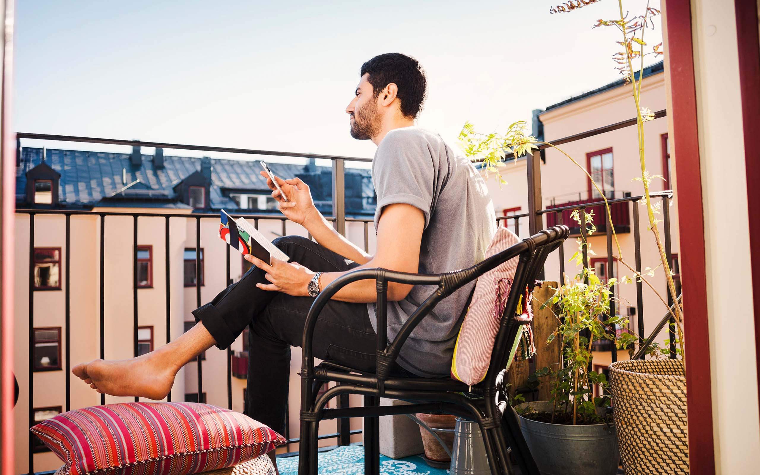 Ein Mann sitzt mit einem Buch und einem Handy in der Hand auf dem Balkon