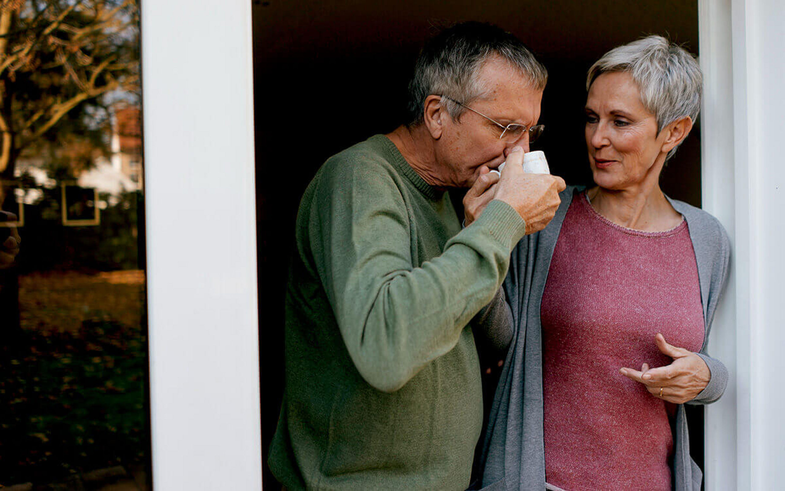 Ein älteres Ehepaar steht in der Terassentür und trinkt Kaffee