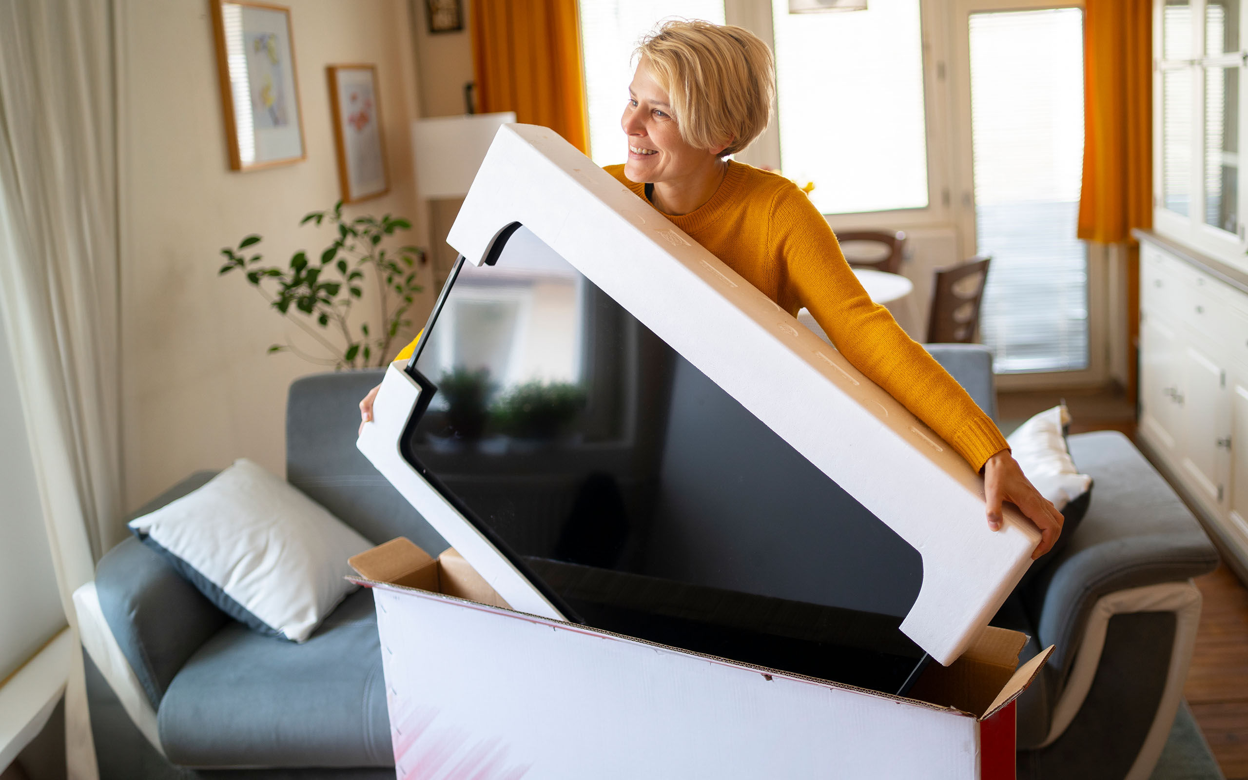 Eine Frau packt hocherfreut einen neuen Fernseher aus dem Versandkarton aus