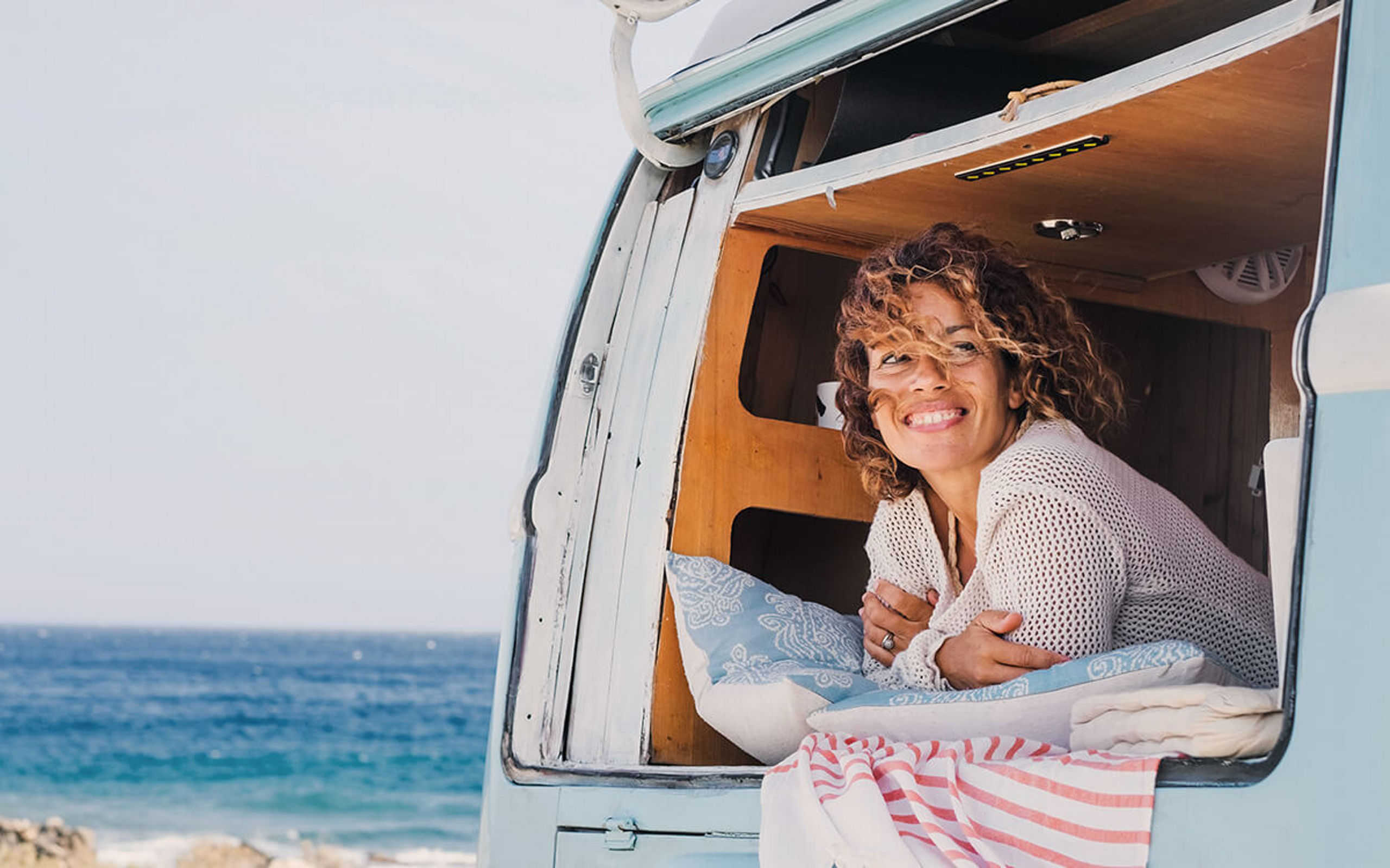 Eine Frau sieht aus einem Wohnmobil, das an einem Strand steht