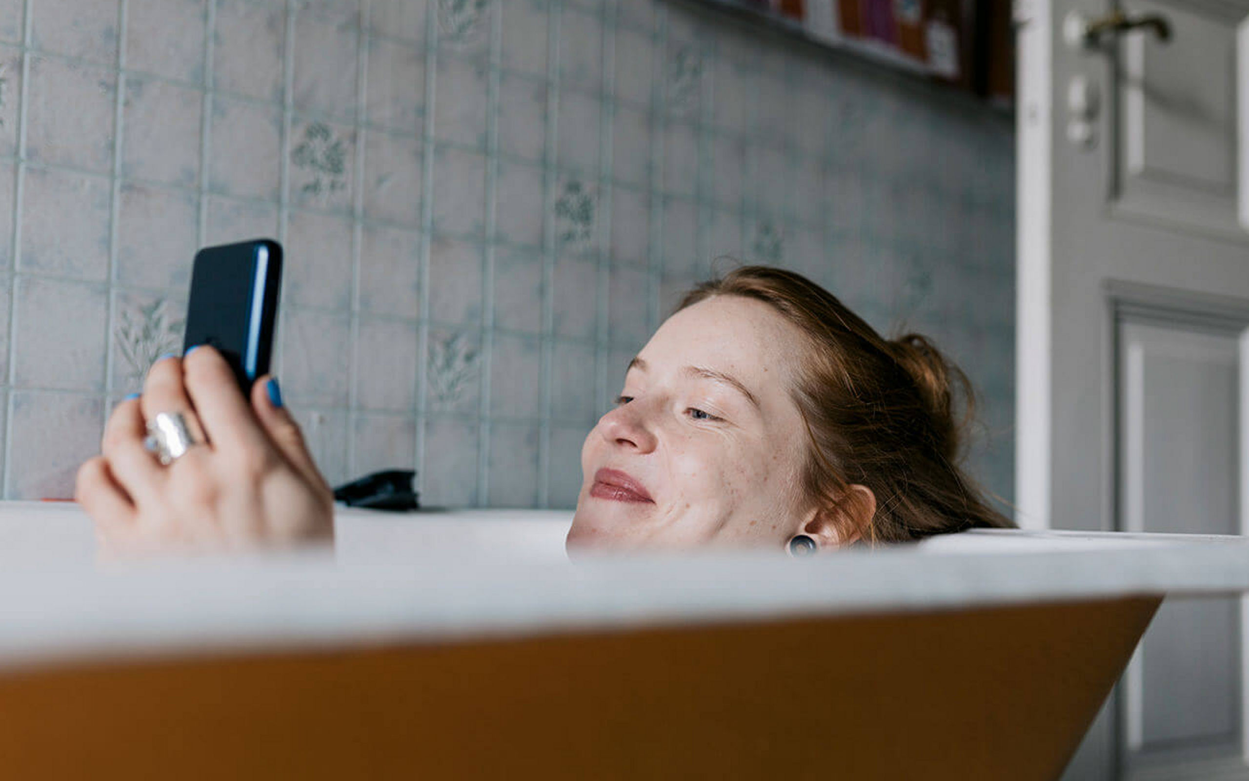 Eine Frau liegt in der Badewanne und schaut auf ihr Smartphone