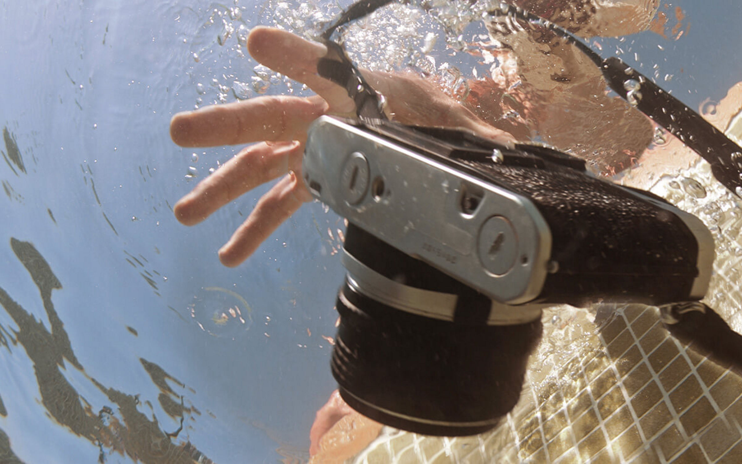 Eine Fotoapparat ist ins Wasser gefallen und eine Hand versucht danach zu greifen