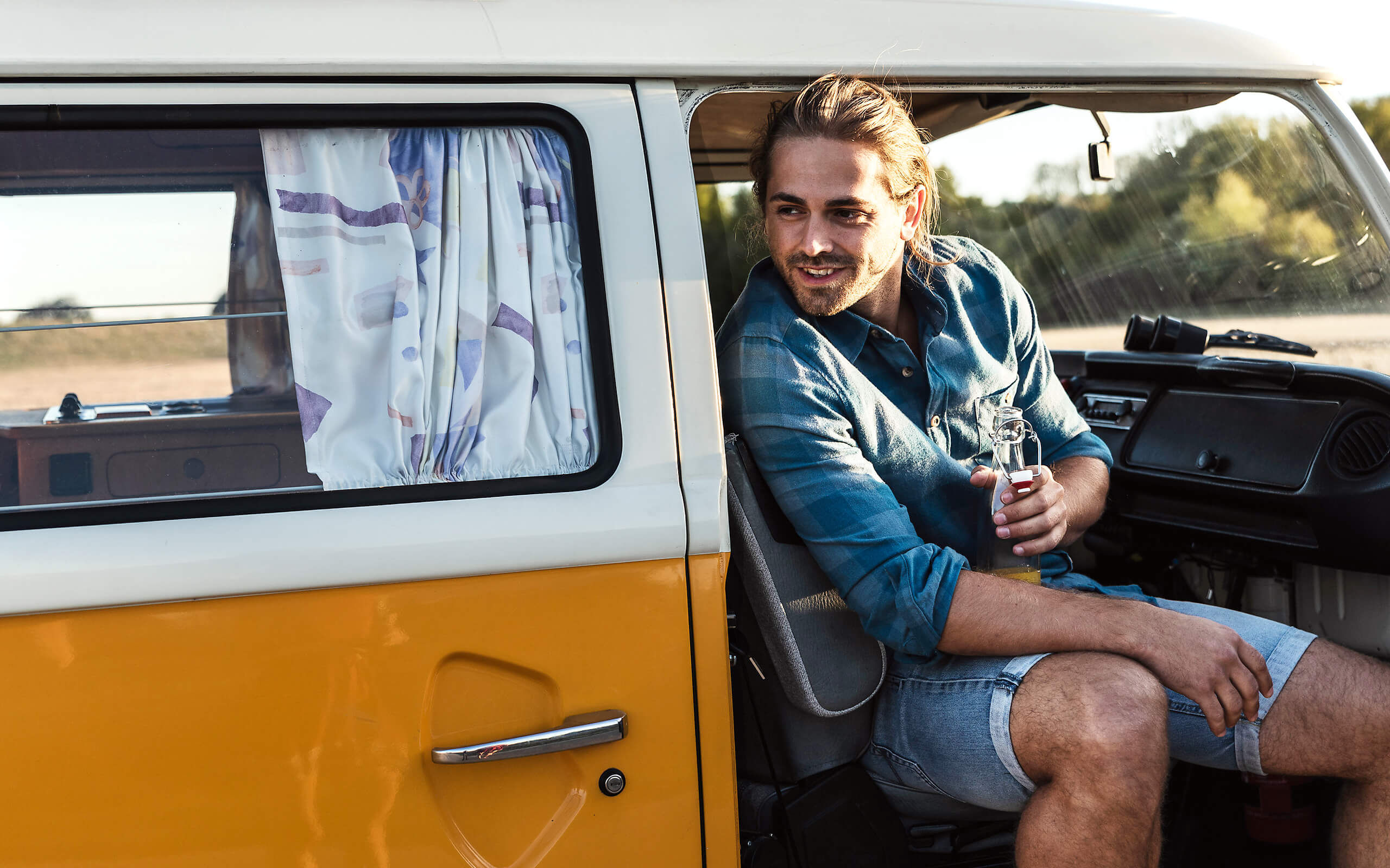 Eine junger Mann sitzt in einem alten VW-Bus und lächelt