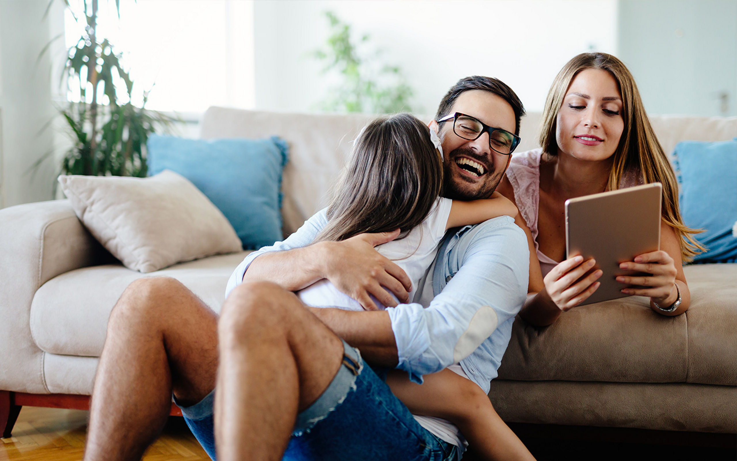 Eine junge, glückliche Familie sitzt auf der Couch und sieht auf ein Laptop