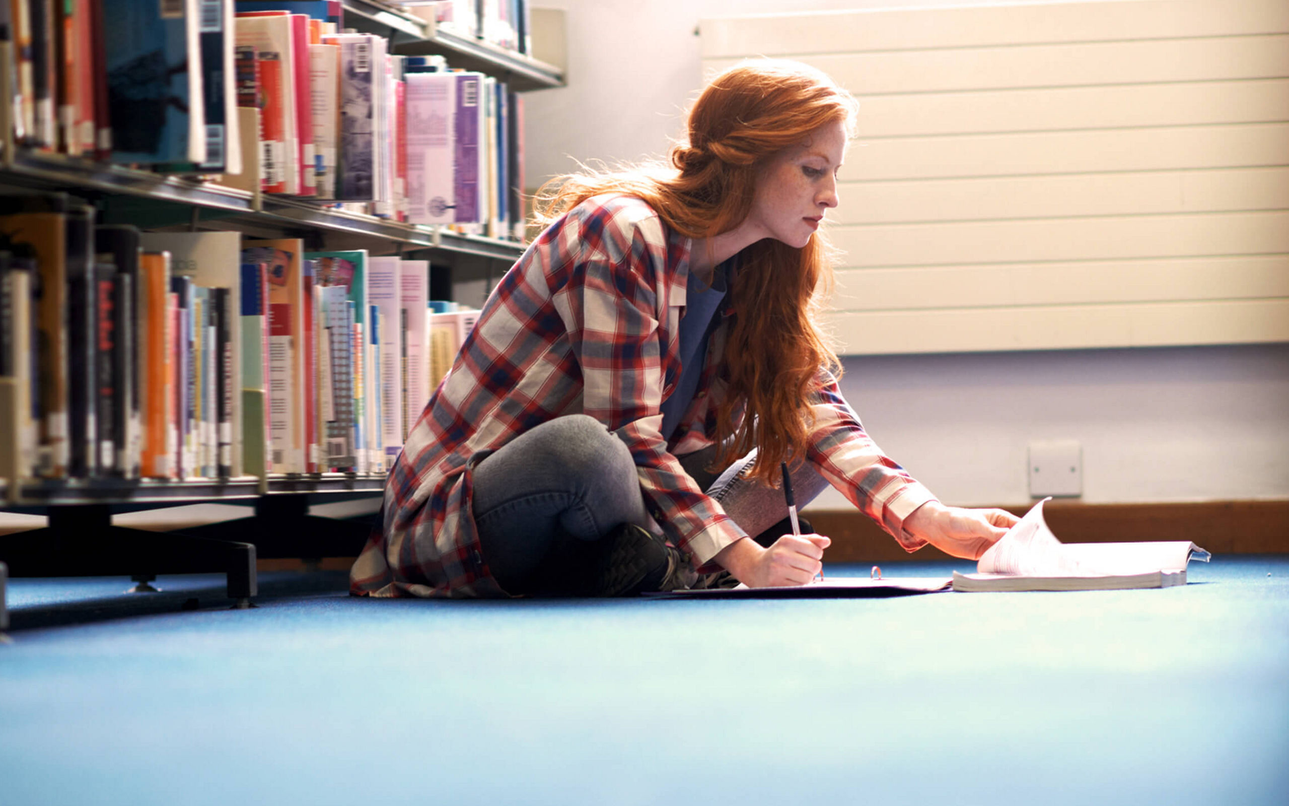 Eine Studentin sitzt auf dem Boden einer Bibliothek und lernt