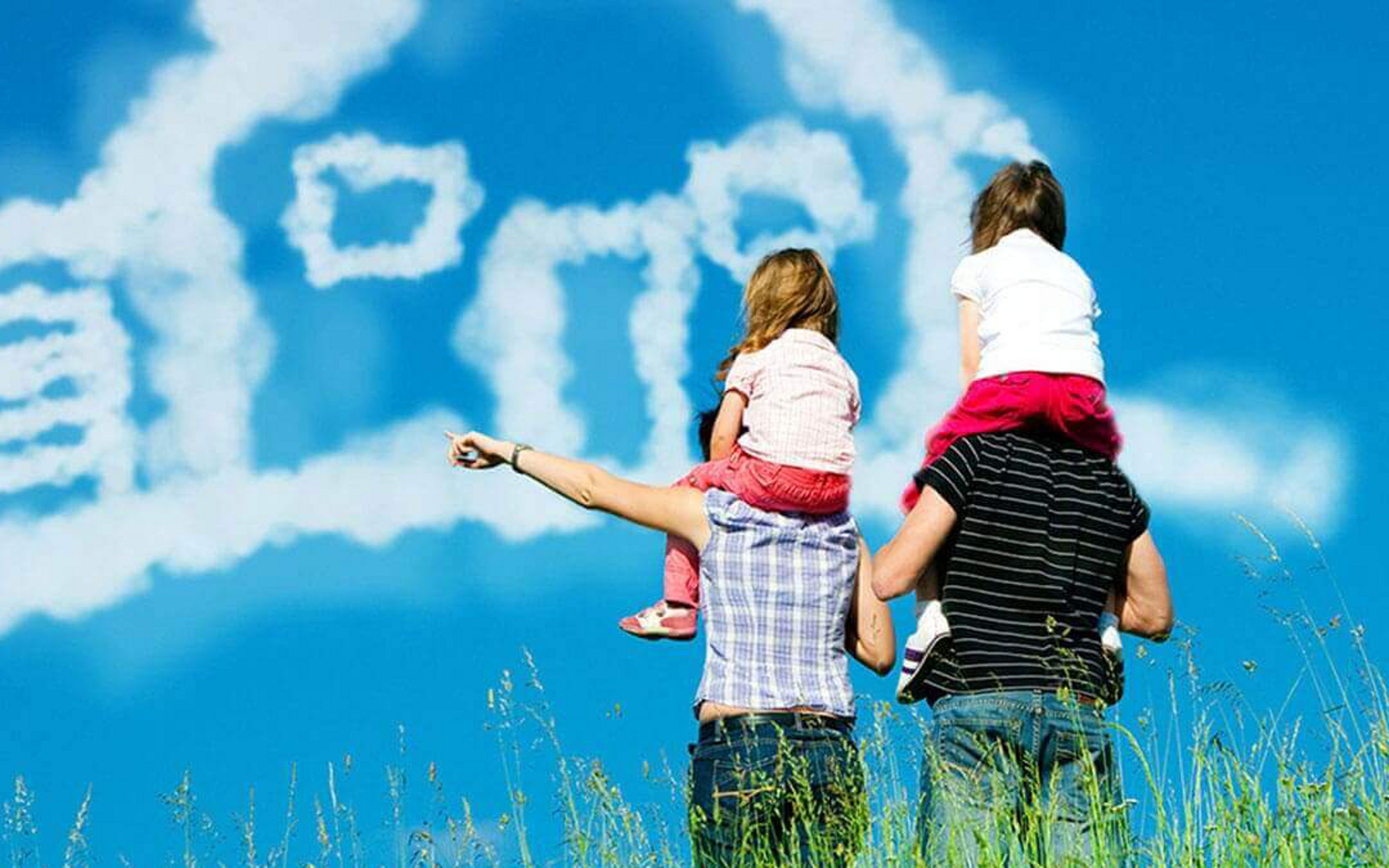 Ein Paar mit zwei Kindern auf den Schultern schaut auf Wolken, die ein Haus darstellen