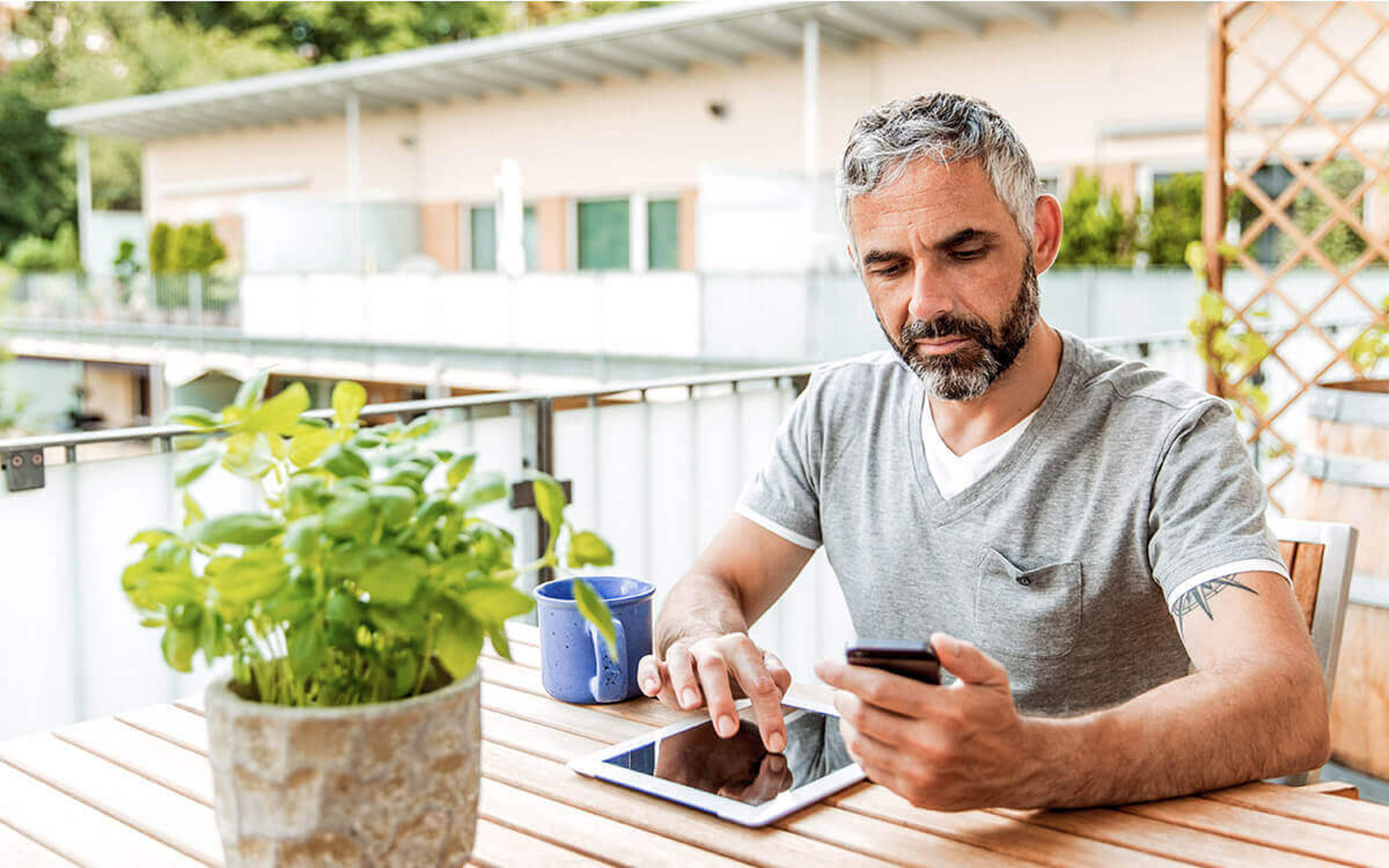 Ein Mann mit Handy und Tablet in der Hand sitzt auf dem Balkon 