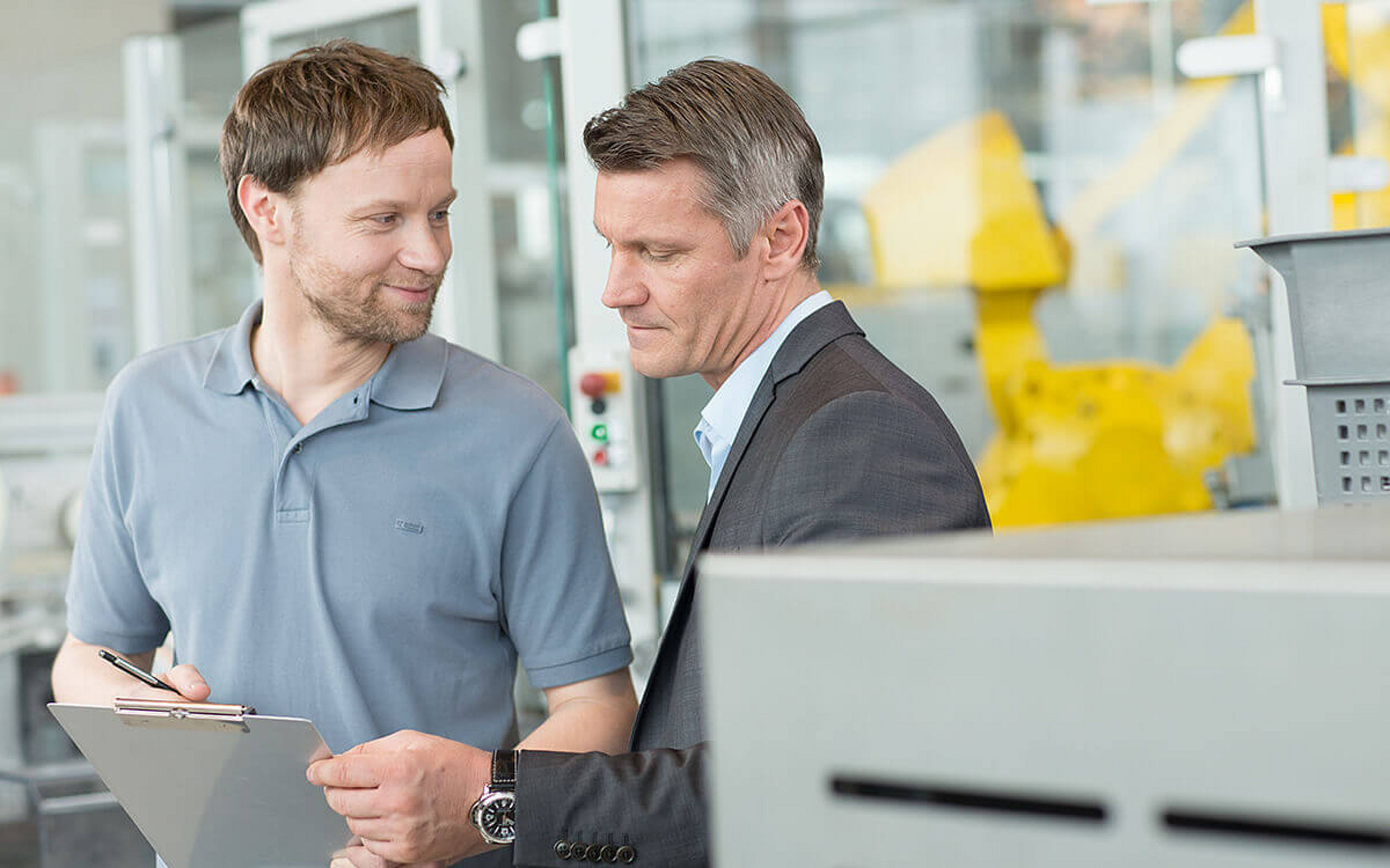 Zwei Männer am Arbeitsplatz sehen auf ein Klemmbrett