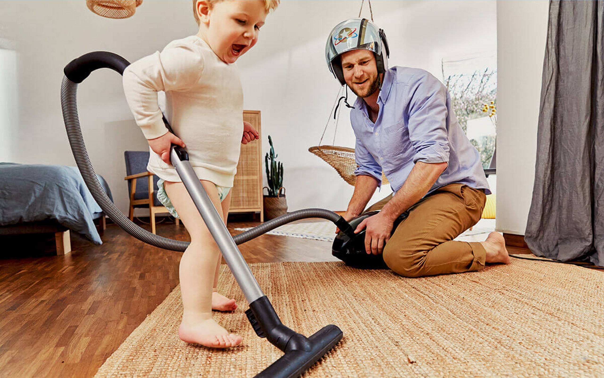 Ein kleiner Junge benutzt einen Staubsauger, der Vater sieht zu