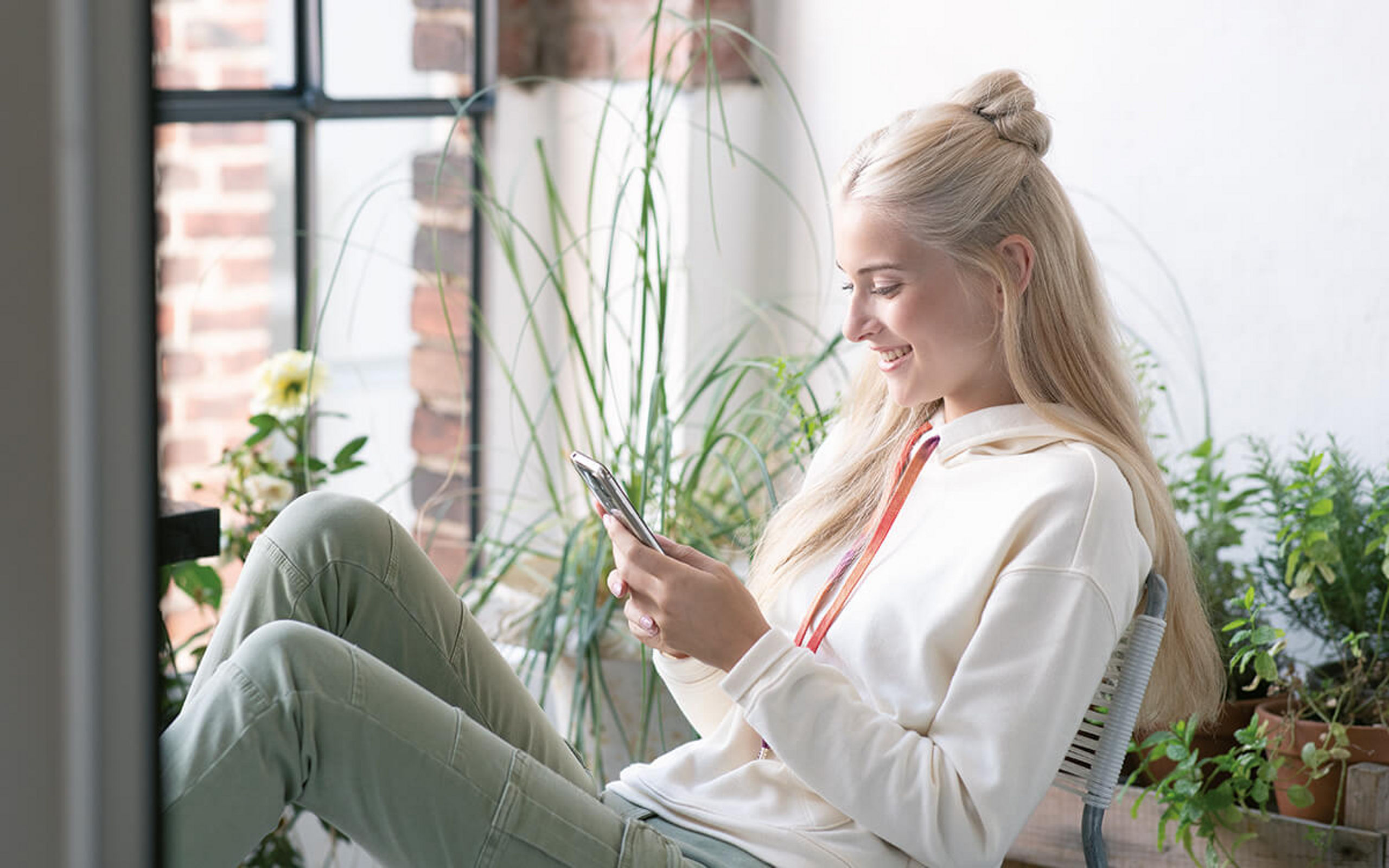 Eine Frau sitzt lächelnd am Fenster und sieht auf ihr Handy